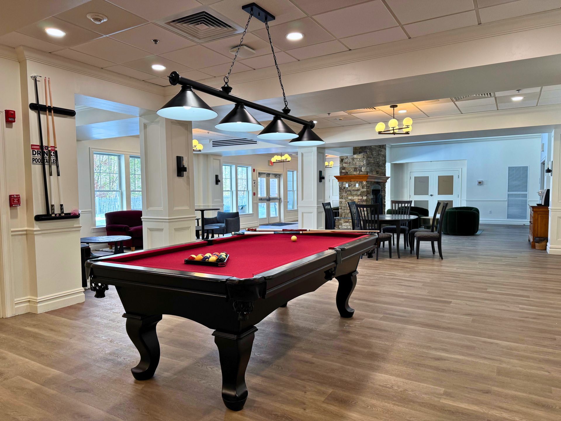 A red felt pool table in a well-lit rec room with a hanging light fixture and various seating areas.