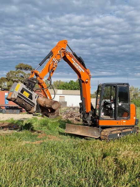 A large orange excavator is sitting in a grassy field.