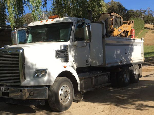 A white truck is parked in a dirt lot with a bulldozer in the back.