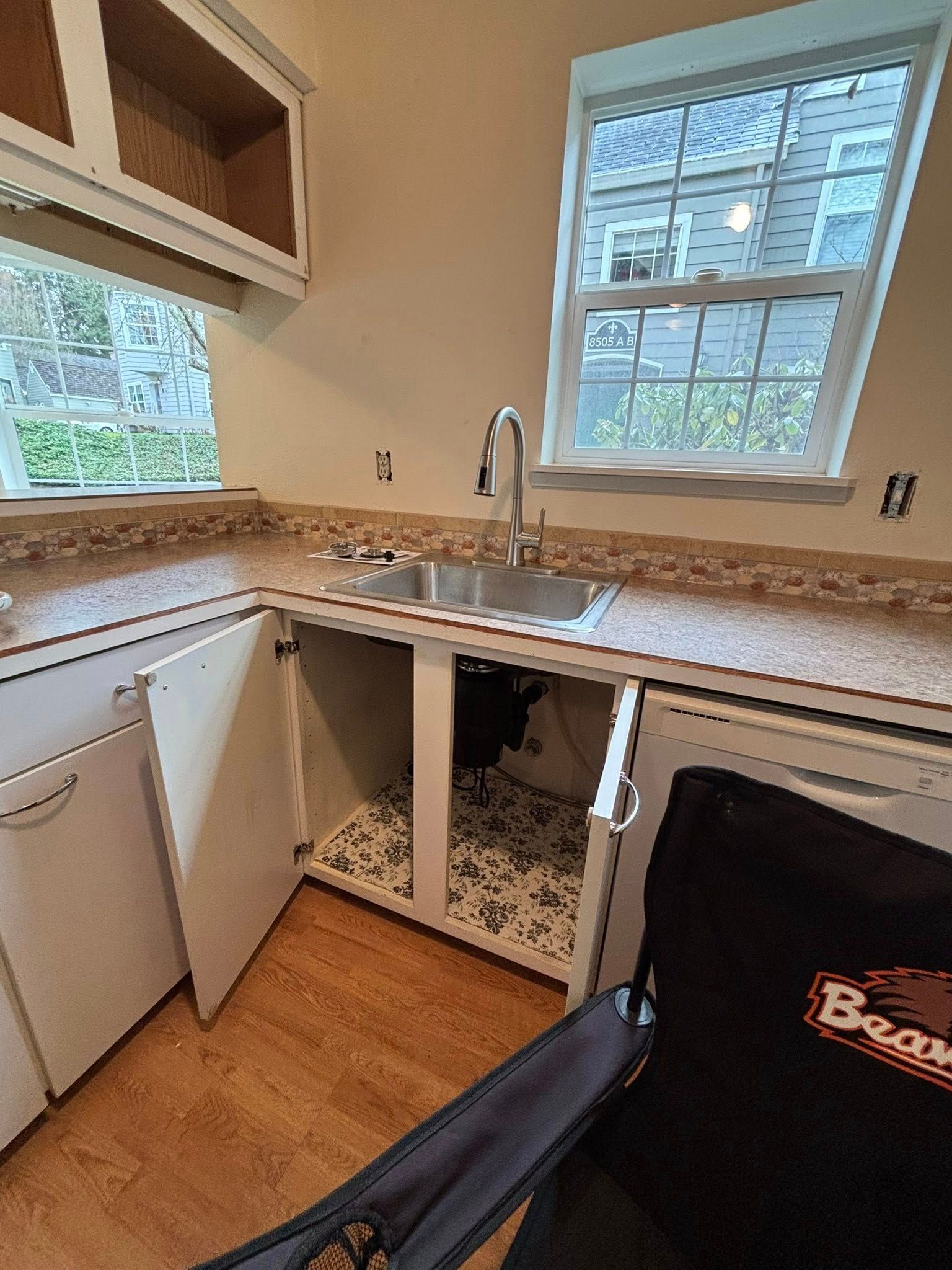 A corner kitchen sink with white cabinets, a chrome faucet, and a black chair in the foreground.