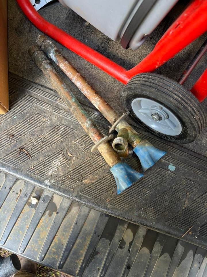 Two copper pipes with blue plastic fittings lying on a dark, ribbed rubber floor mat next to a red wheel.