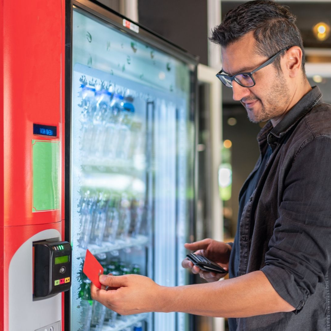 Man using a red card to pay for a drink at a vending machine.