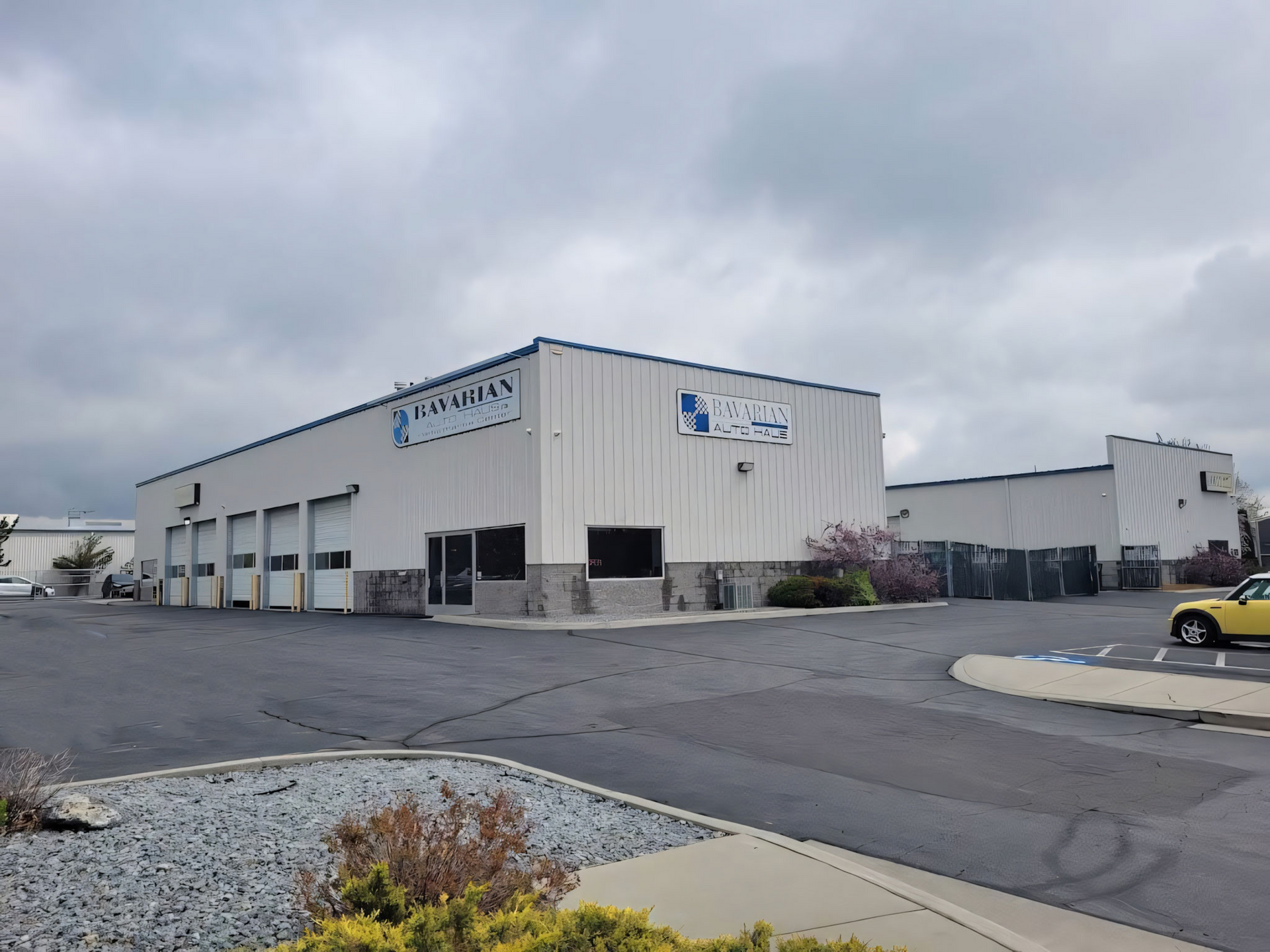 White industrial building with blue trim and signage, cloudy sky. | Bavarian Auto Haus