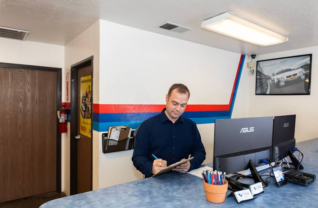 Man writing at a reception desk in an auto repair shop. Blue and red stripe on the wall. | Bavarian Auto Haus