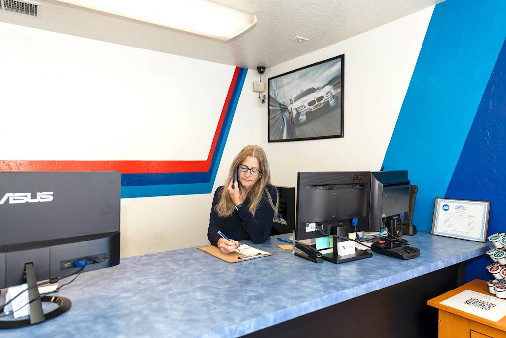 A woman at a reception desk talking on the phone. The office has blue, white, and red decor. | Bavarian Auto Haus