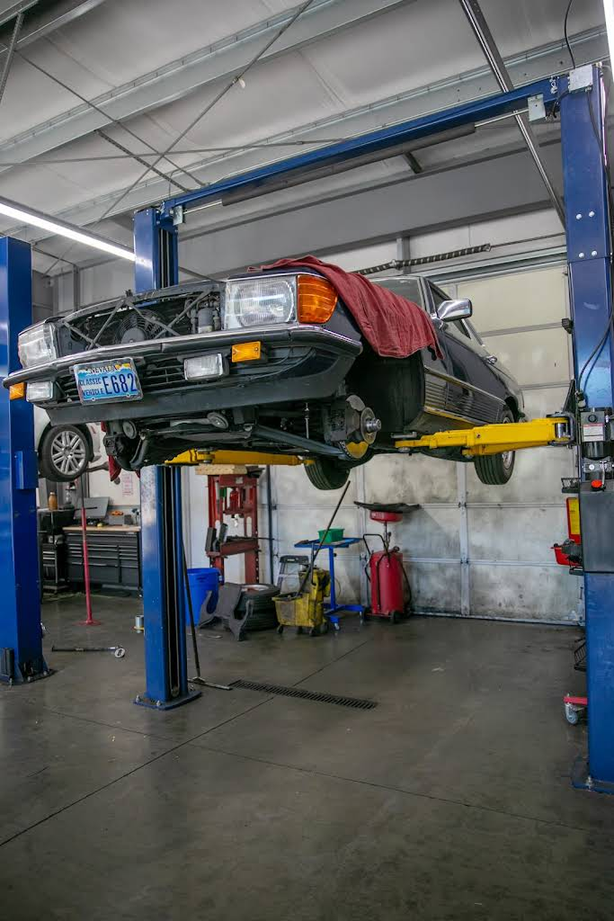Black car raised on a blue automotive lift inside a garage; front end being worked on. | Bavarian Auto Haus
