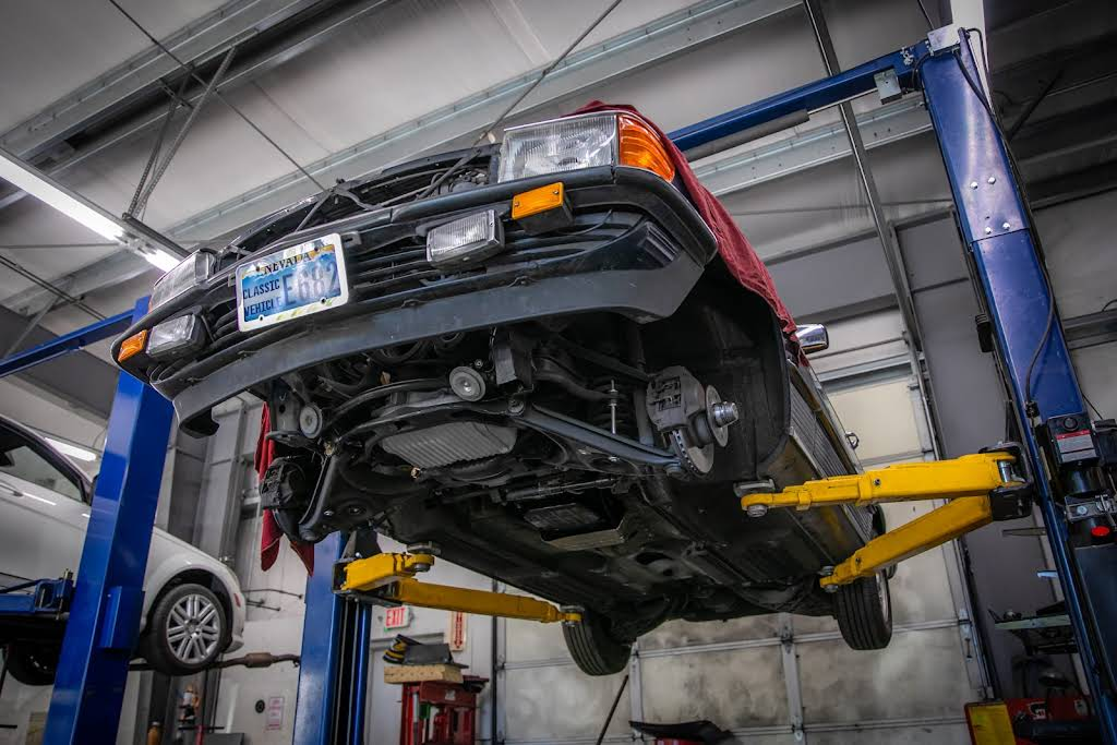Red car raised on a lift in a garage, undercarriage visible. | Bavarian Auto Haus