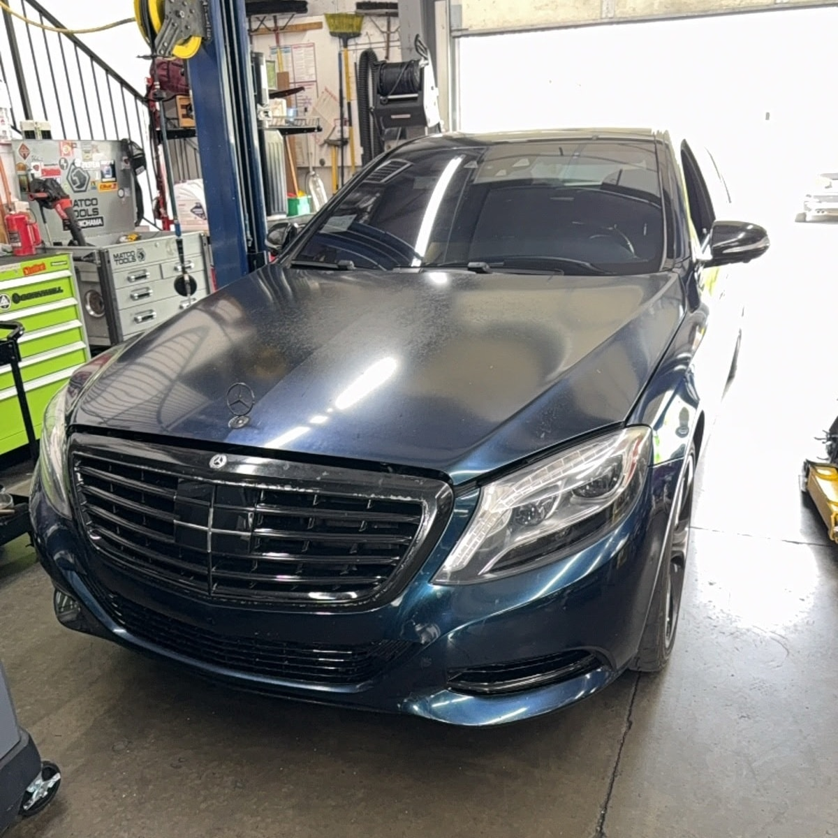 Blue Mercedes sedan in a repair shop, hood up, in front of a raised lift. | Bavarian Auto Haus