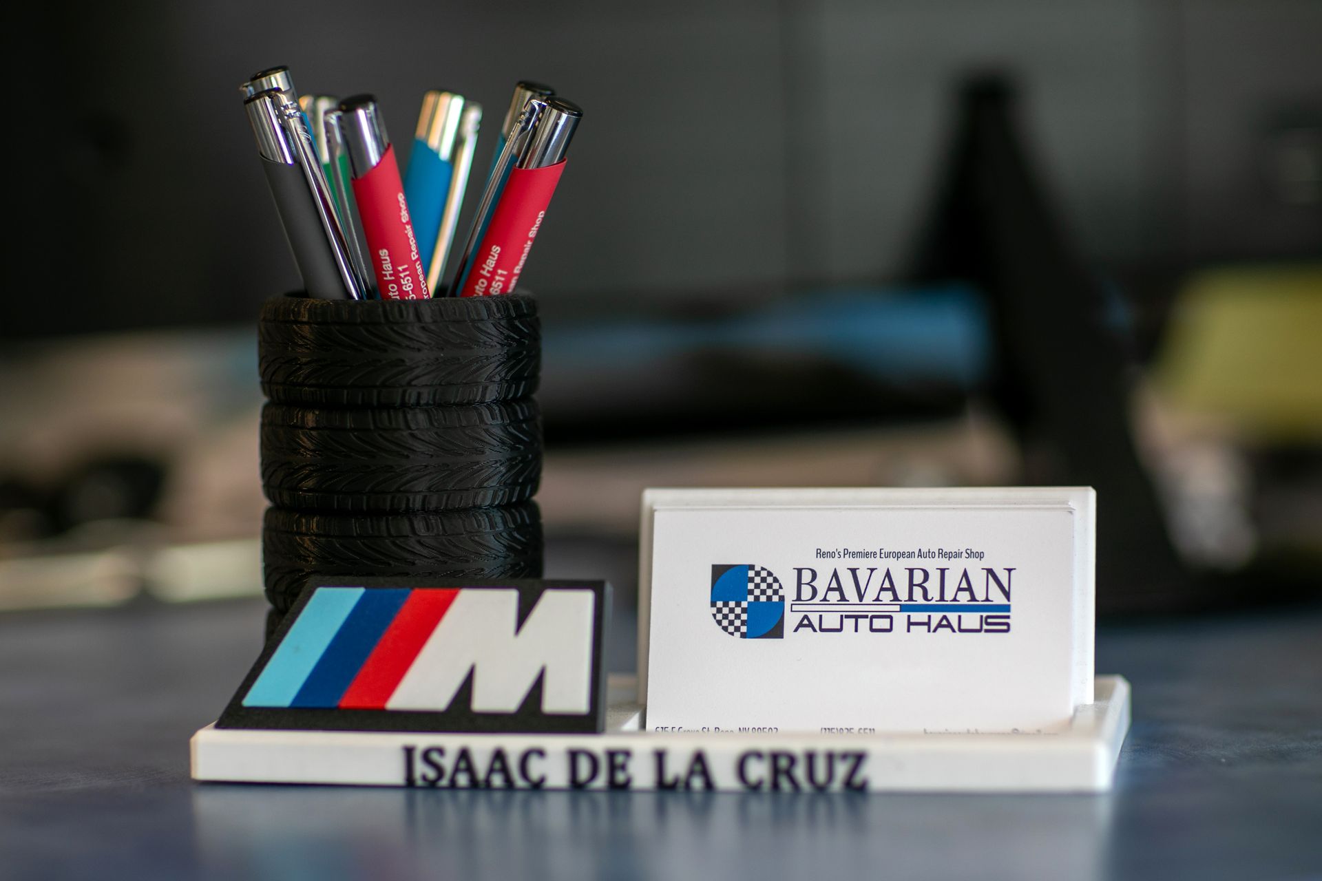 A desk organizer with a tire-shaped pen holder, BMW M logo, and a business card for Isaac de la Cruz at Bavarian Auto Haus. | Bavarian Auto Haus
