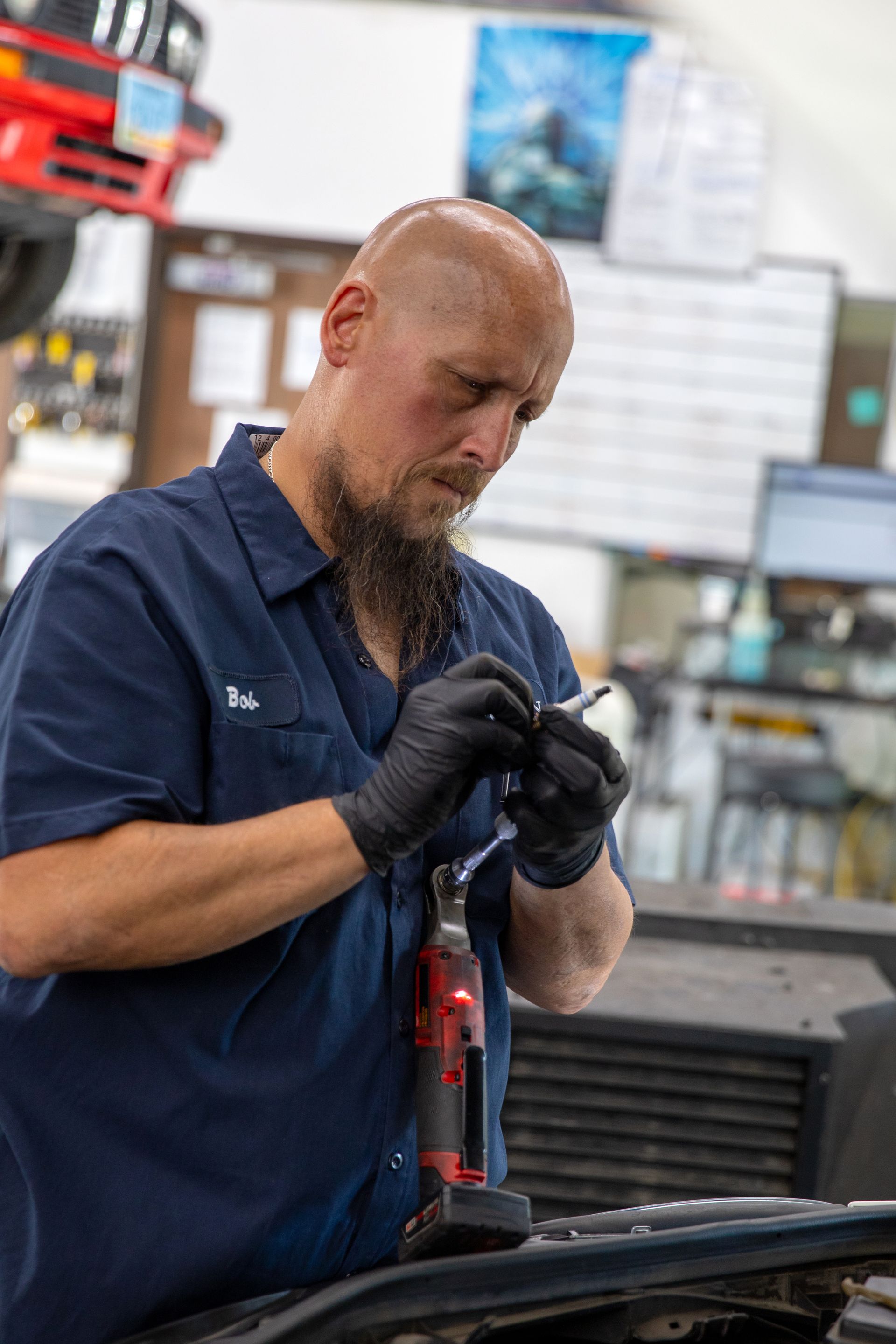 A focused technician in a blue uniform and black gloves works on a car part in an auto repair shop. | Bavarian Auto Haus