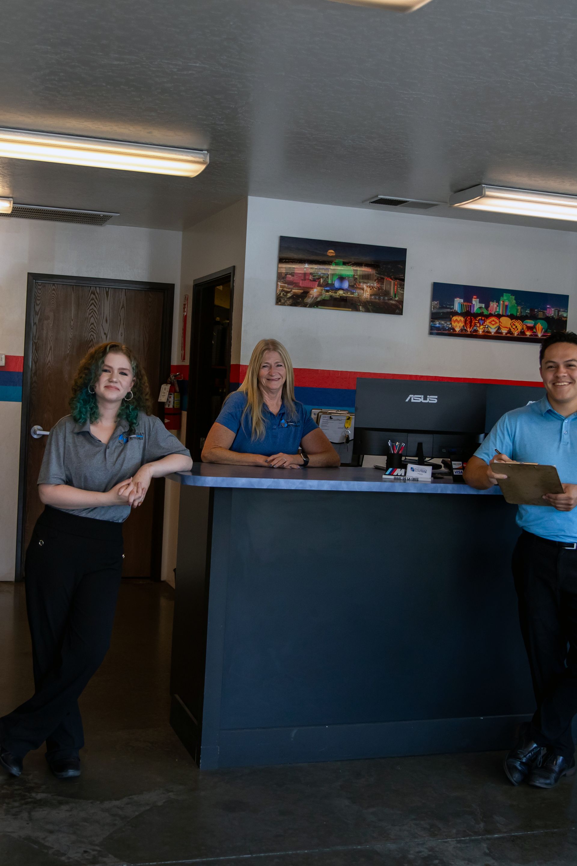 Three people stand behind and around a reception desk in an office setting, smiling at the camera. | Bavarian Auto Haus