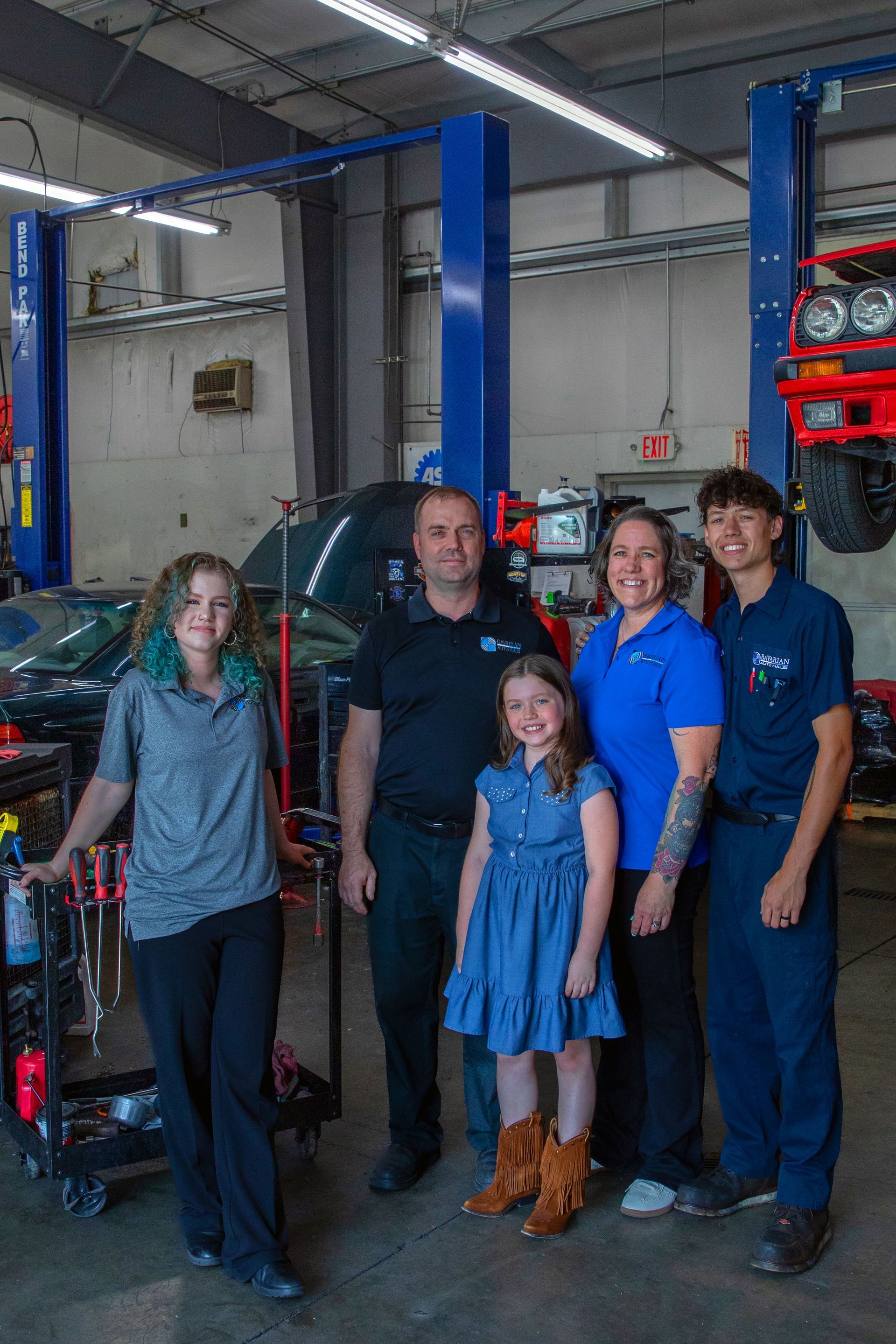 A family stands together in an automotive repair shop, posing in front of vehicle lifts and tools. | Bavarian Auto Haus