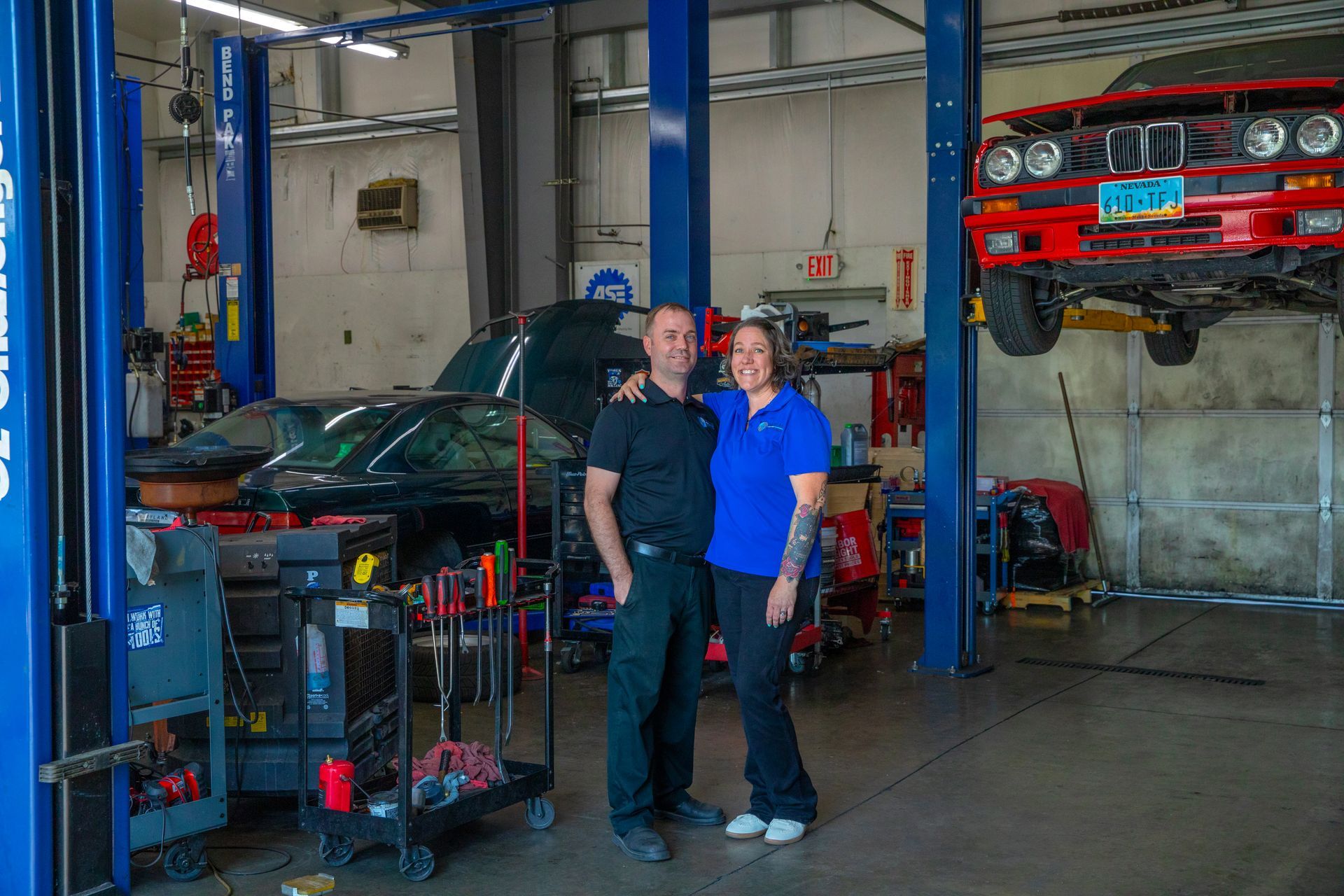 Two people standing in an auto repair shop with a car on a lift in the background. | Bavarian Auto Haus