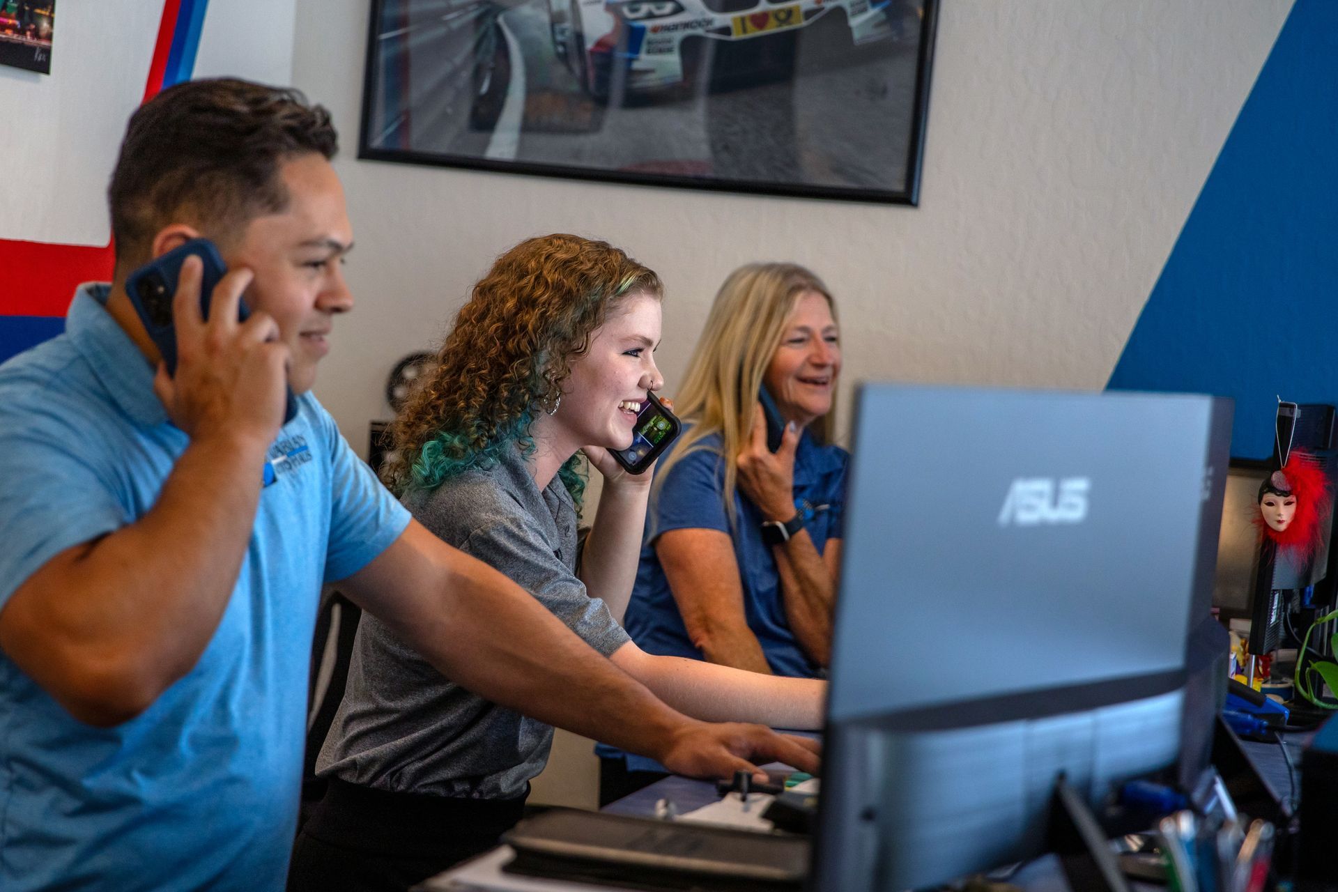 Three people in an office work at desks while talking on their phones. | Bavarian Auto Haus