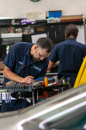 Mechanic smiling, holding tablet, wearing blue uniform, and standing in a garage. | Bavarian Auto Haus
