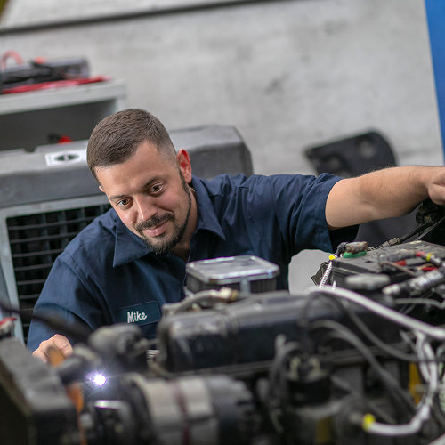Mechanic in blue work shirt, inspecting vehicle engine in a garage. | Bavarian Auto Haus
