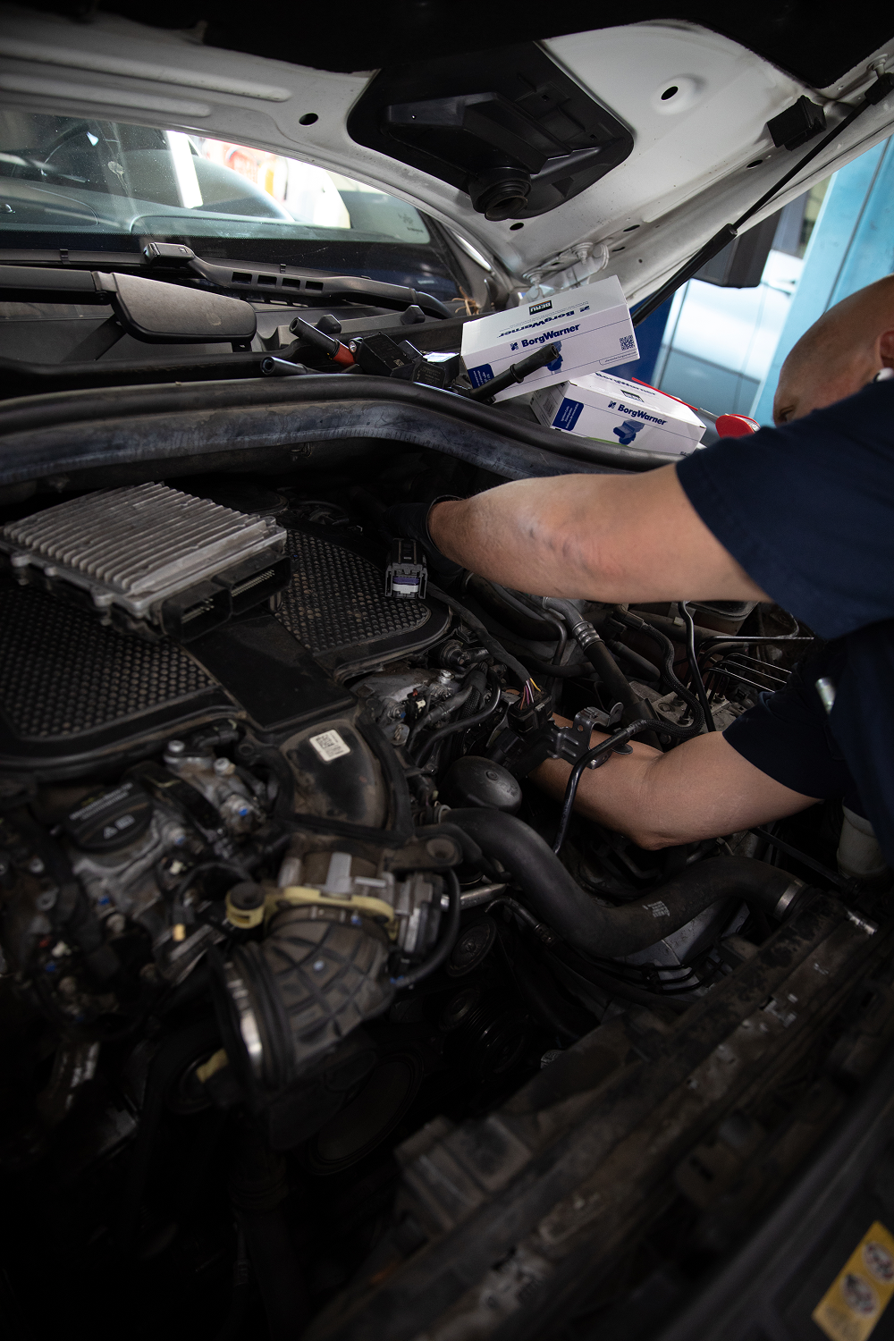 Mechanic working on a car engine under the hood; open workspace. | Bavarian Auto Haus