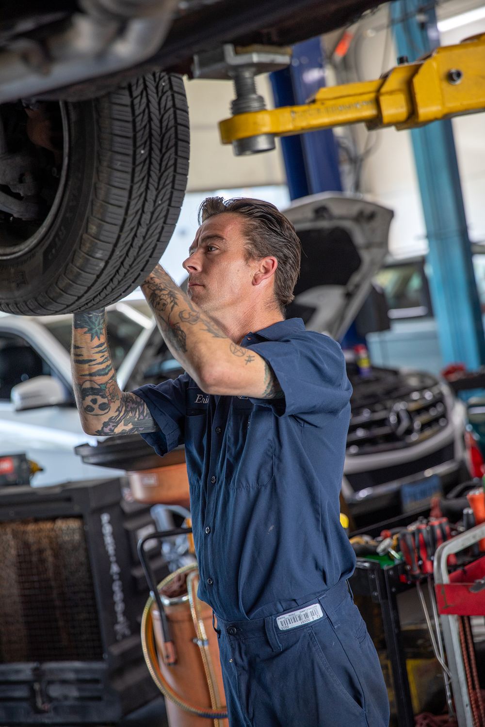 Mechanic in blue jumpsuit works on car raised by a lift inside a garage. | Bavarian Auto Haus