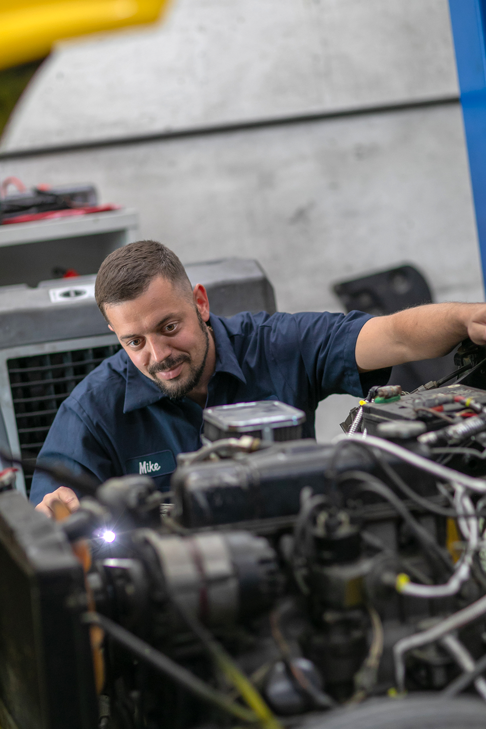 Mechanic in blue work shirt, working on car engine, workshop setting. | Bavarian Auto Haus