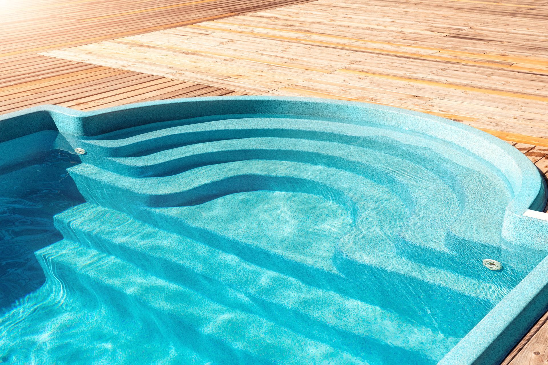 Turquoise swimming pool with curved steps beside a tan tiled deck
