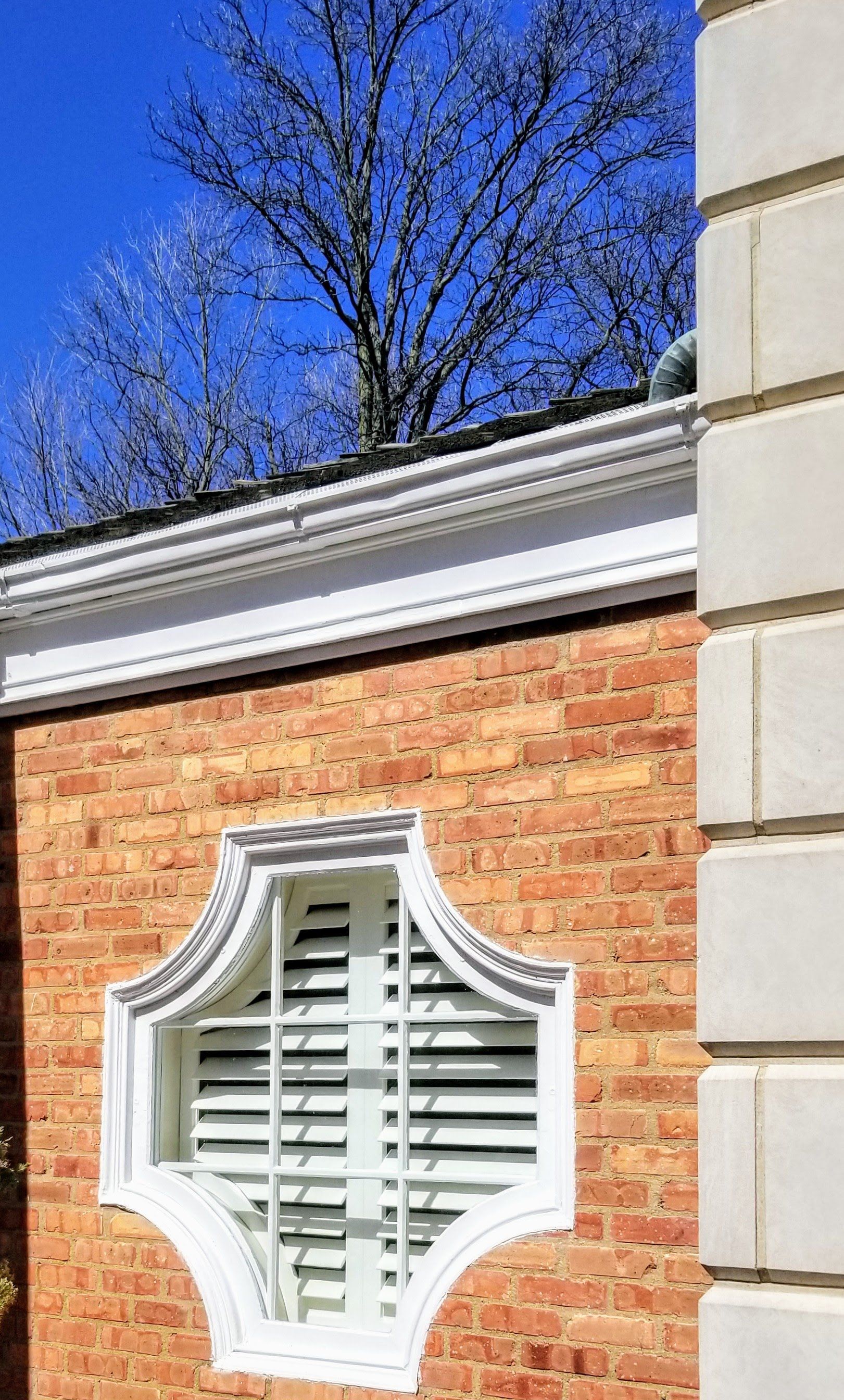 specialty shaped window with a solar shield plantation shutter installed on it, looking at it from outside a home