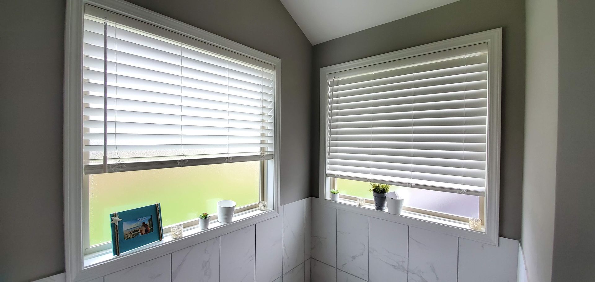 A bathroom with two windows with blinds on them.
