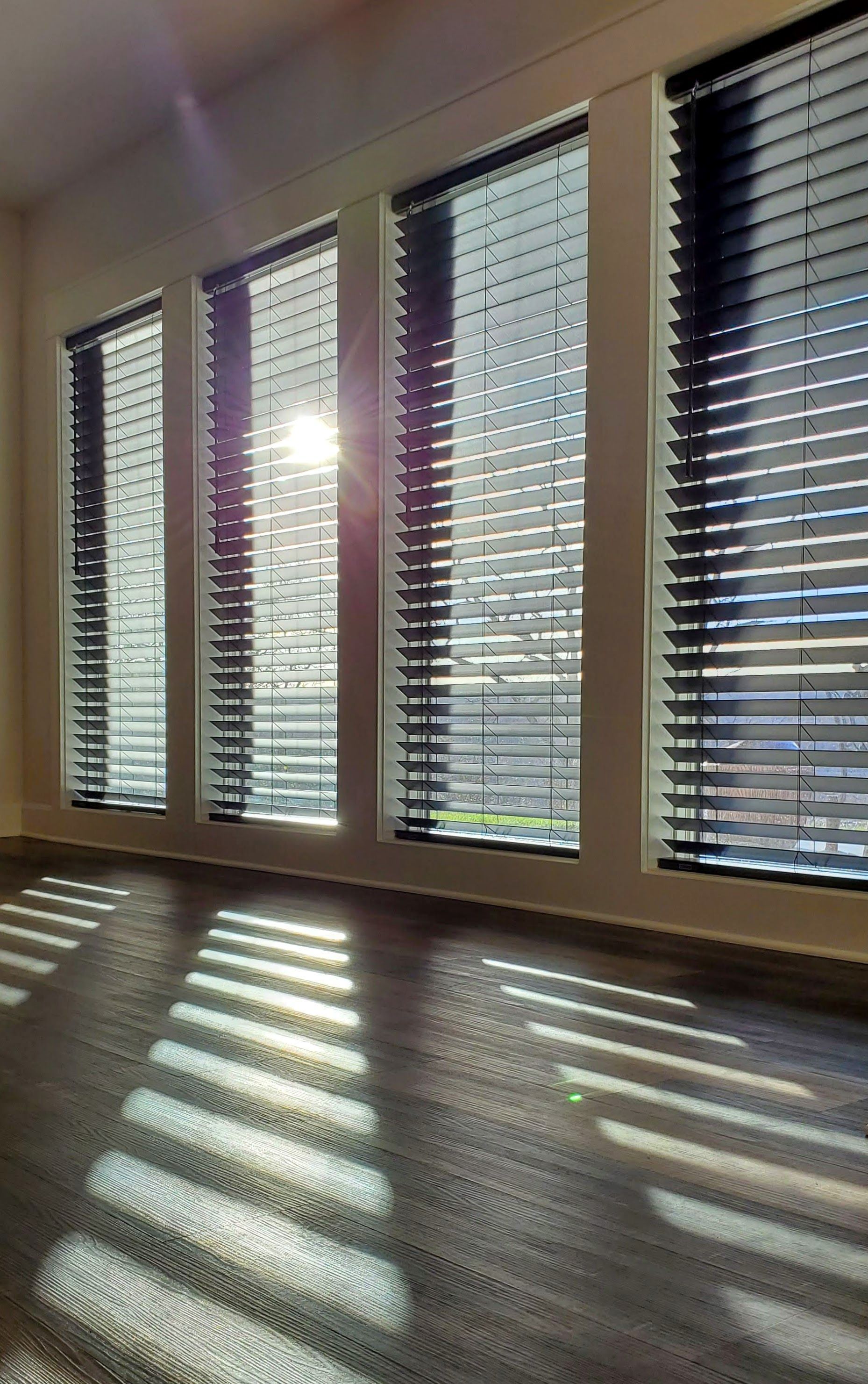 A living room with blinds on the windows and the sun shining through the blinds.