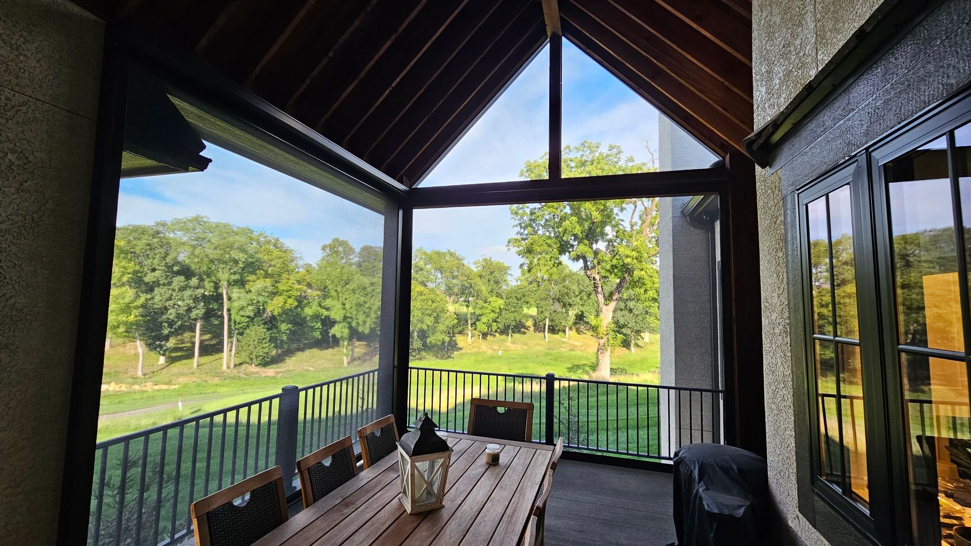 A screened in porch with a table and chairs and a view of a golf course.