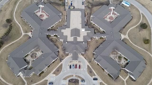 Aerial view of a symmetrical building complex with four square wings, courtyards, and a central entrance with a driveway.