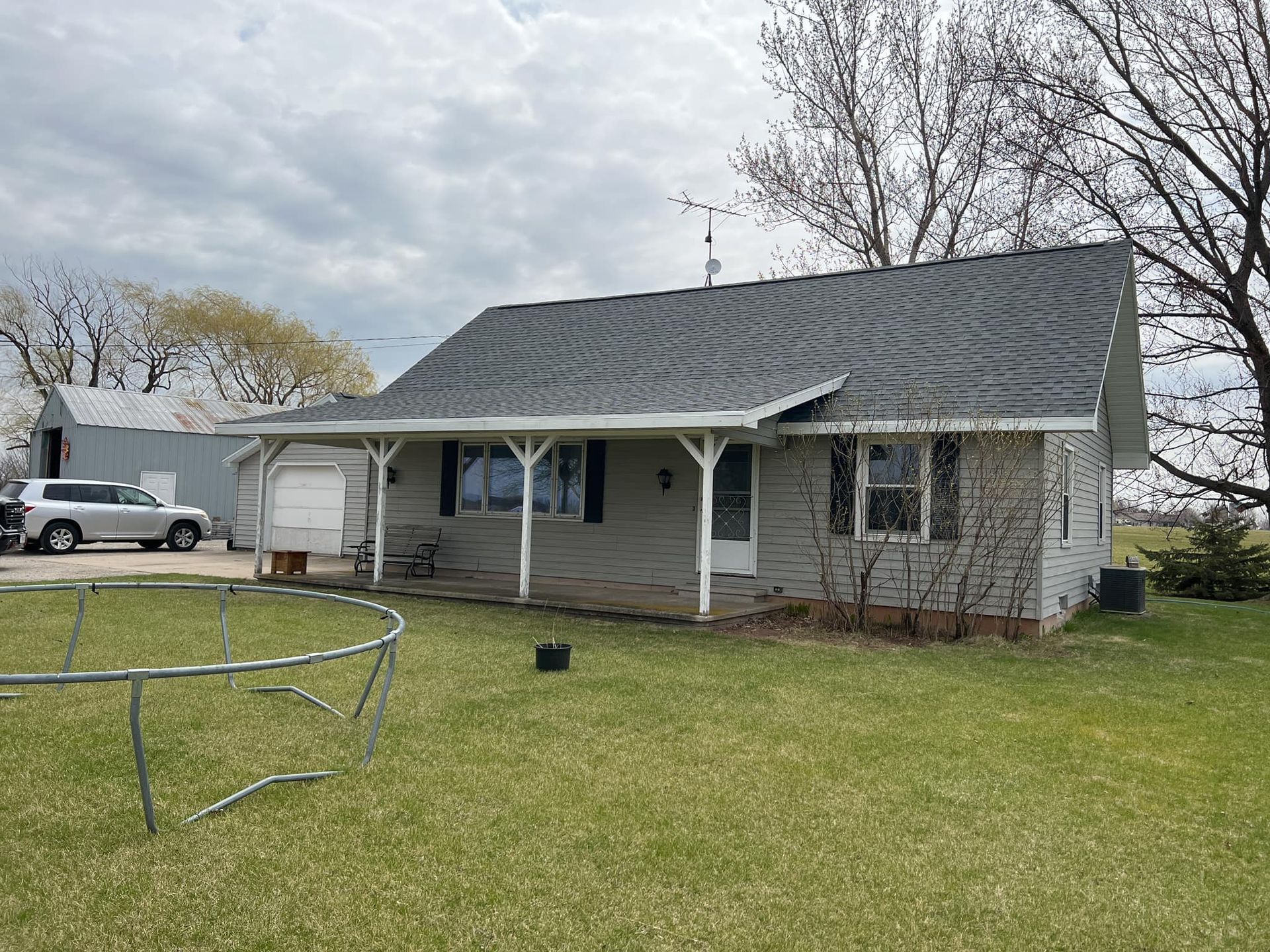 A white house with a porch and a trampoline in front of it.