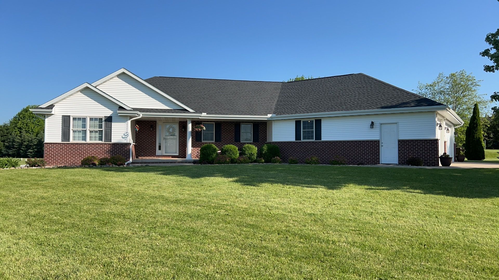 A white house with a black roof is sitting on top of a lush green field.