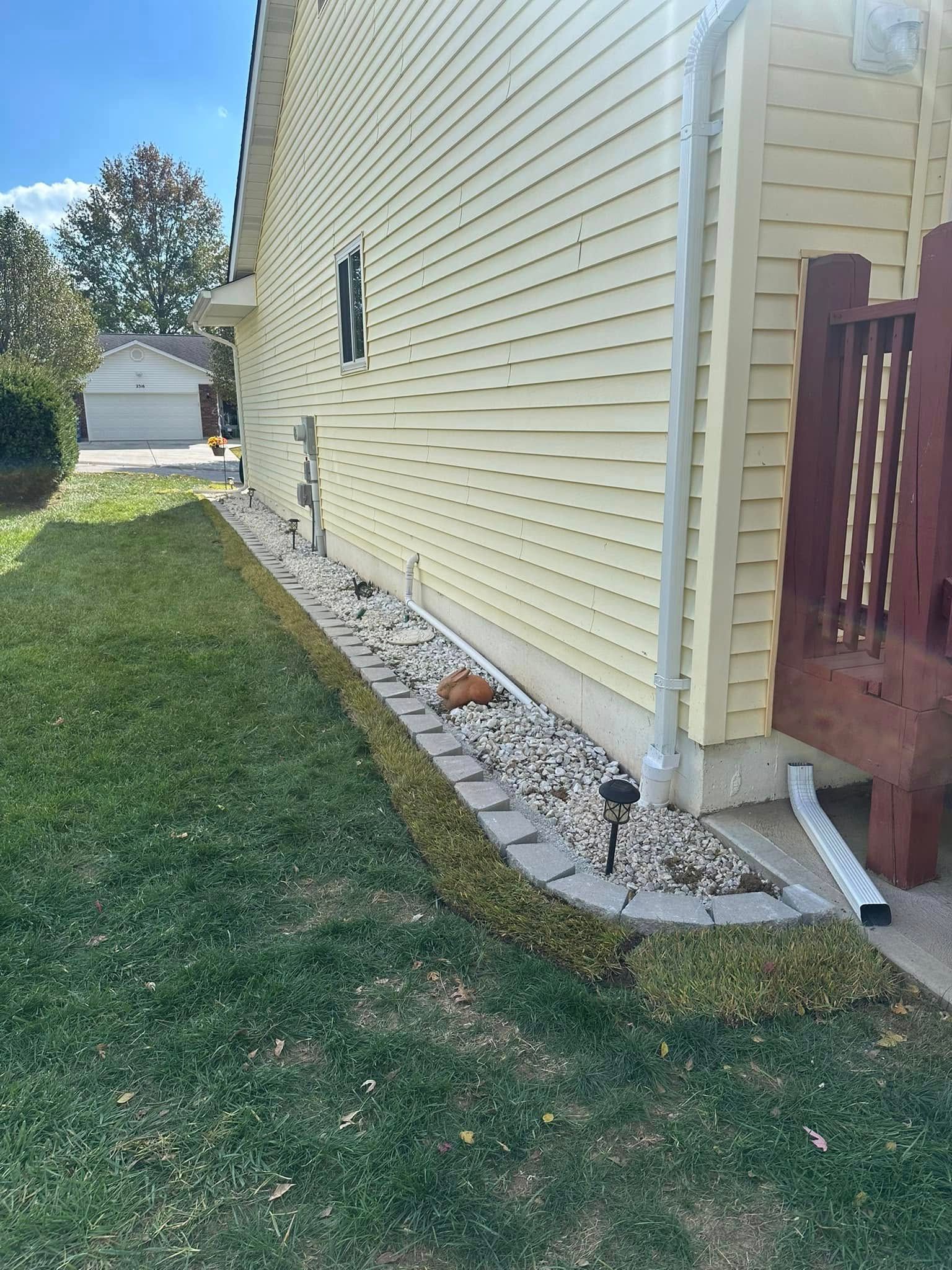 Side view of a yellow house featuring a landscaped rock border and a wooden deck.