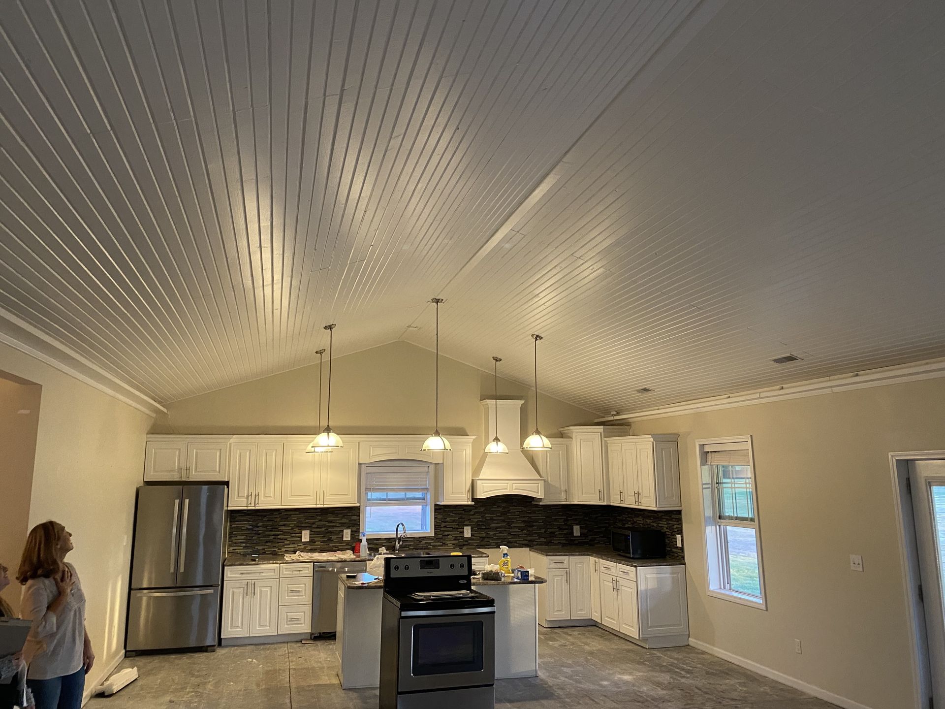 A wide kitchen features white beadboard vaulted ceilings, white cabinets, stainless steel appliances, and tile flooring.