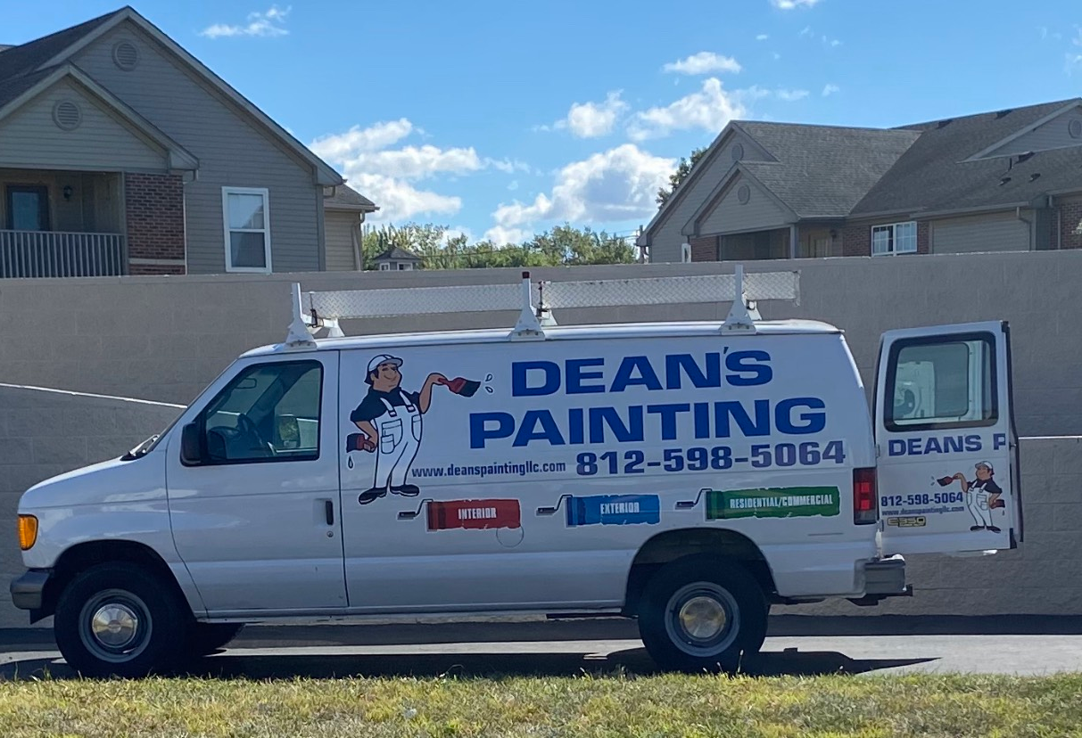 A white Dean's Painting work van with a phone number and mascot parked in front of a tan wall and suburban houses.