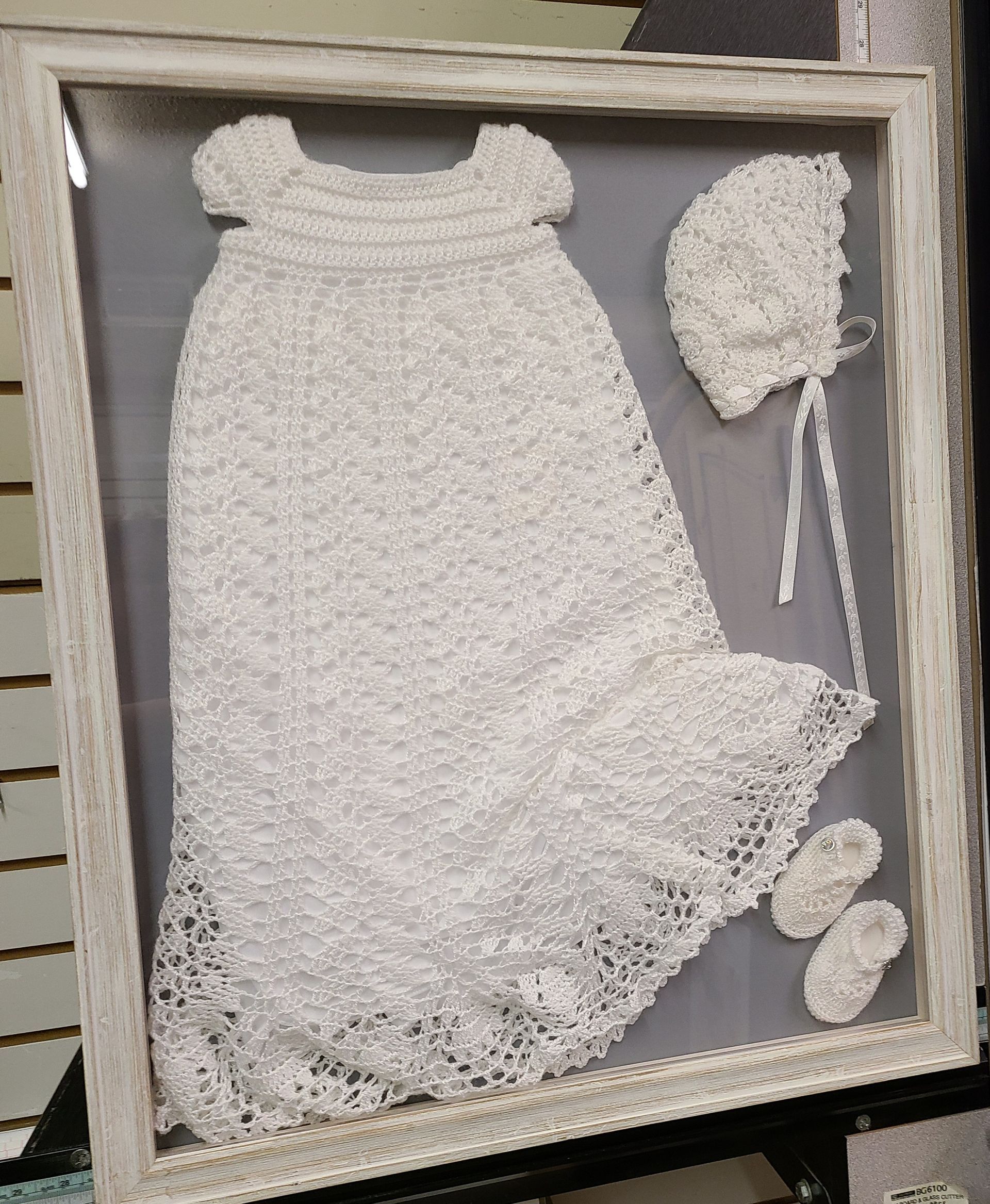 A picture of a crocheted baby dress and hat in a frame.