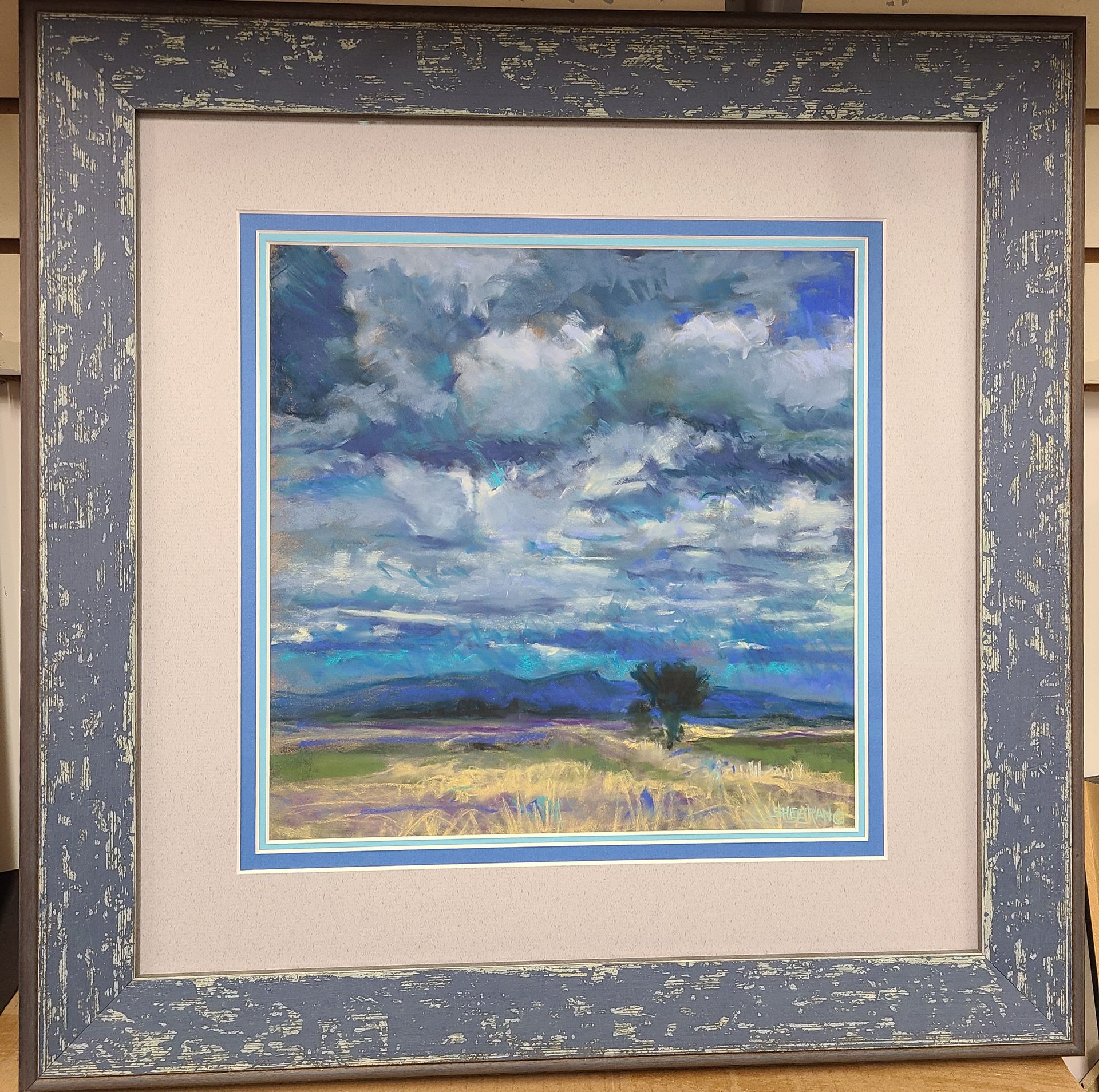 A framed painting of a cloudy sky with a tree in the foreground