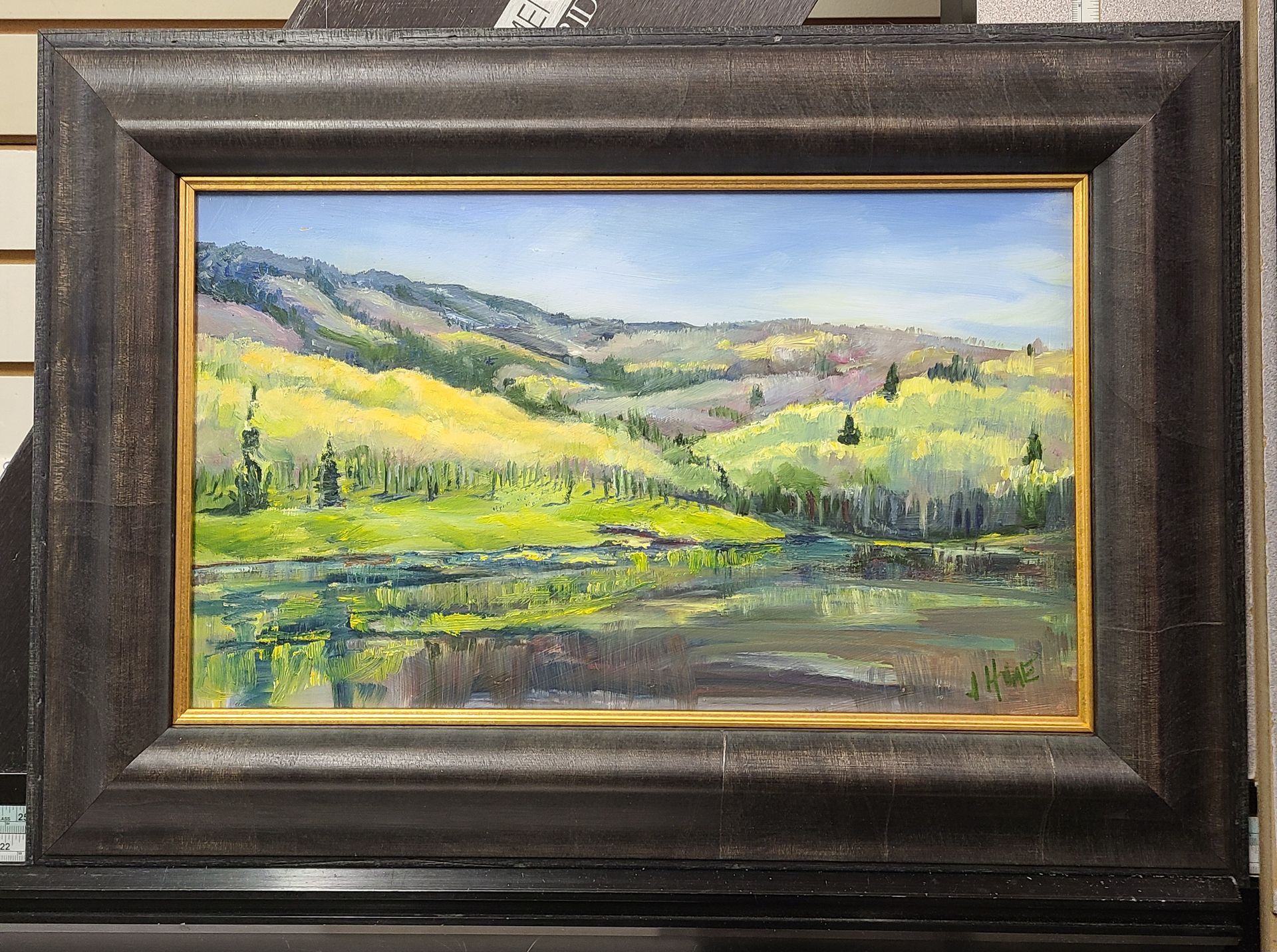 A framed painting of a lake with mountains in the background
