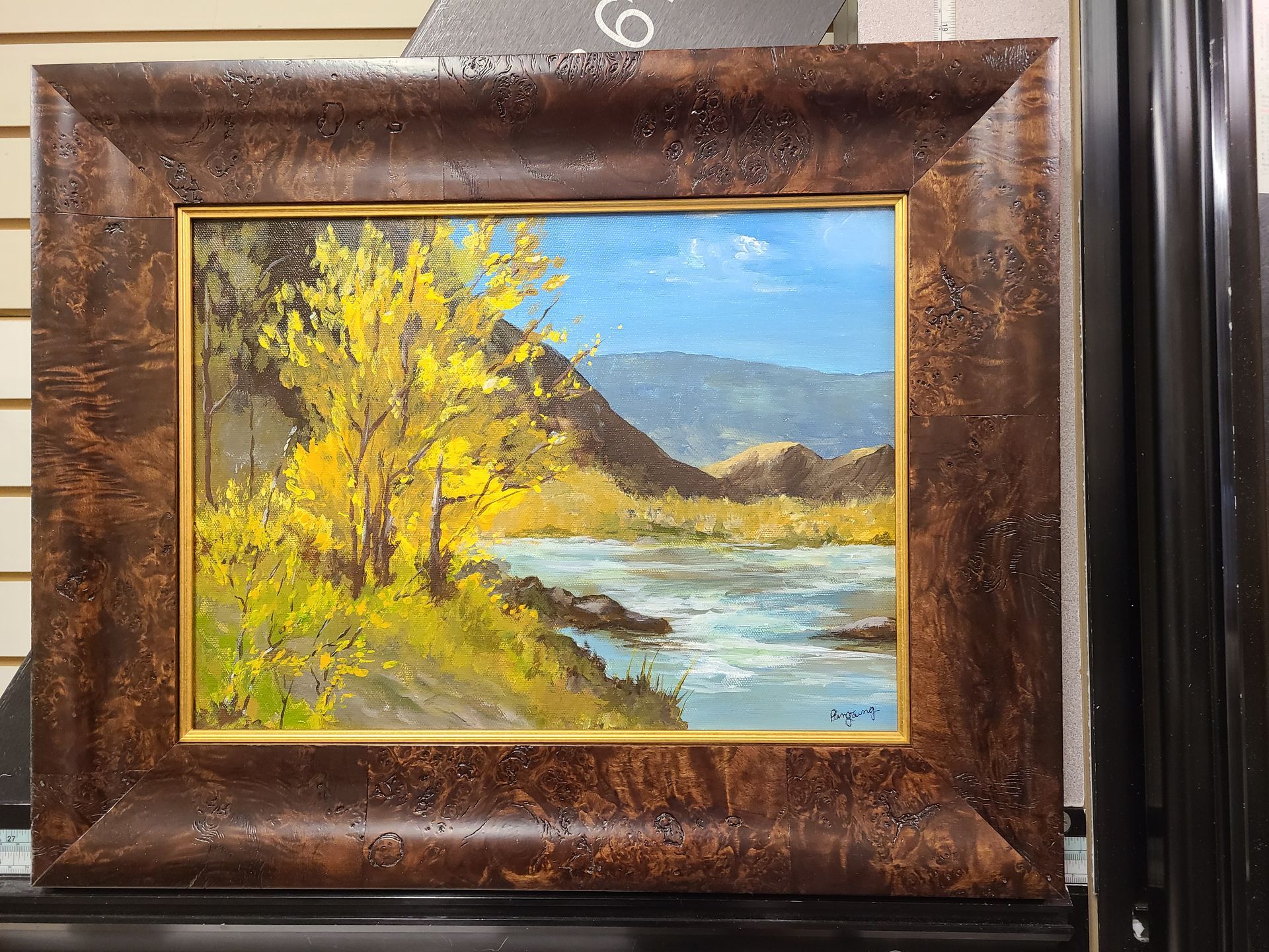 A framed painting of a river with mountains in the background