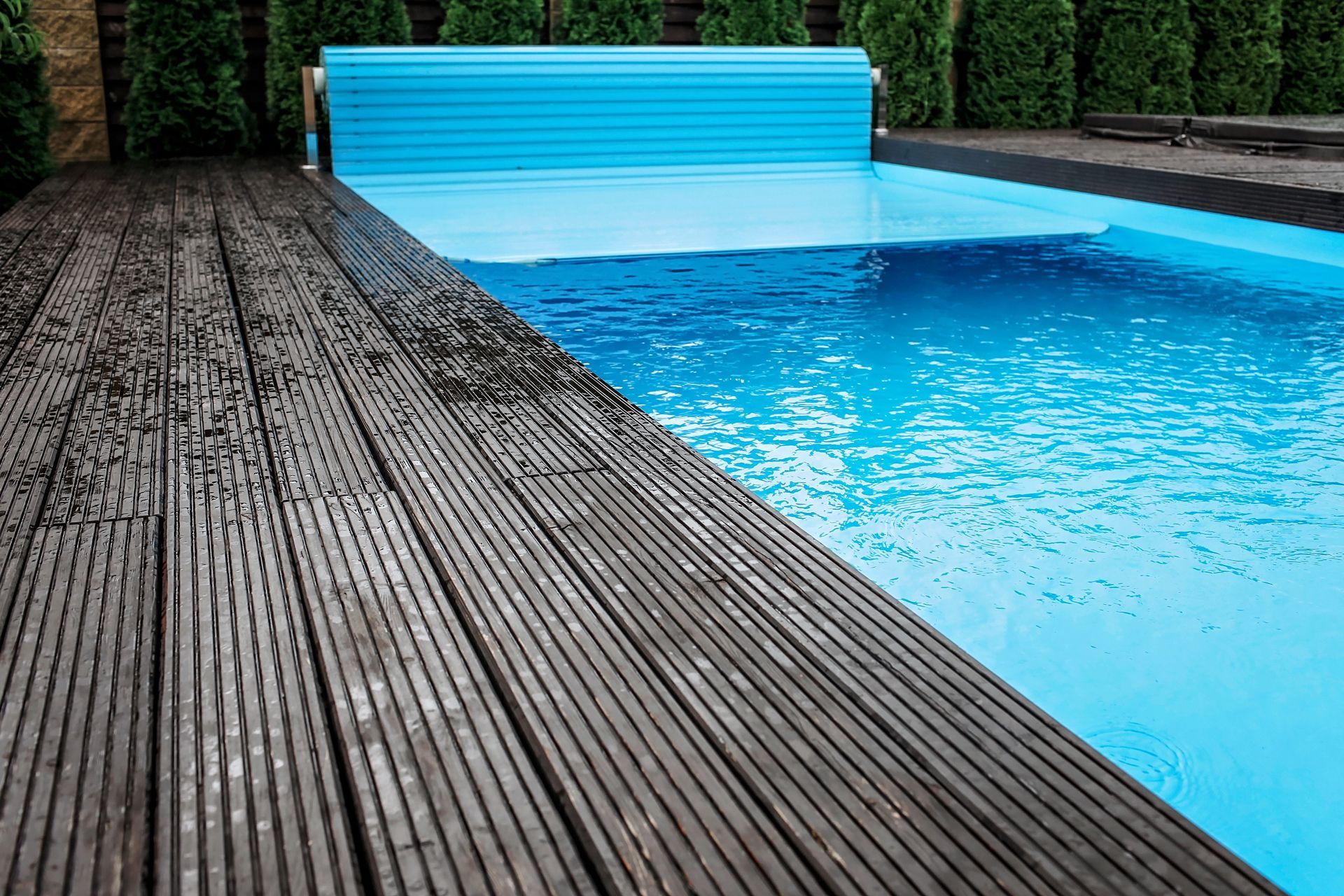 Wooden deck next to a blue swimming pool, partially covered by a blue pool cover.