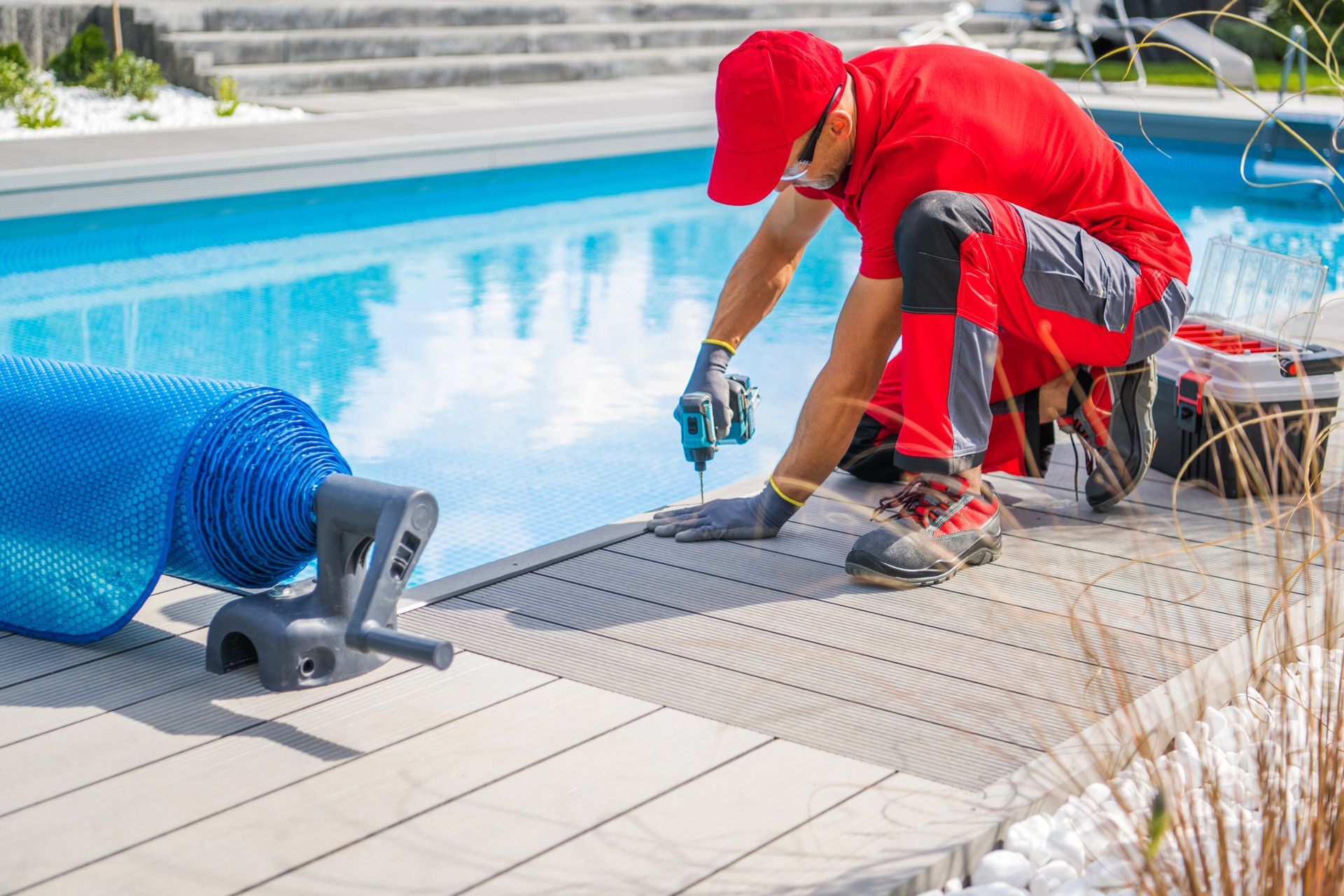 Person in red installing pool cover on deck with blue water.