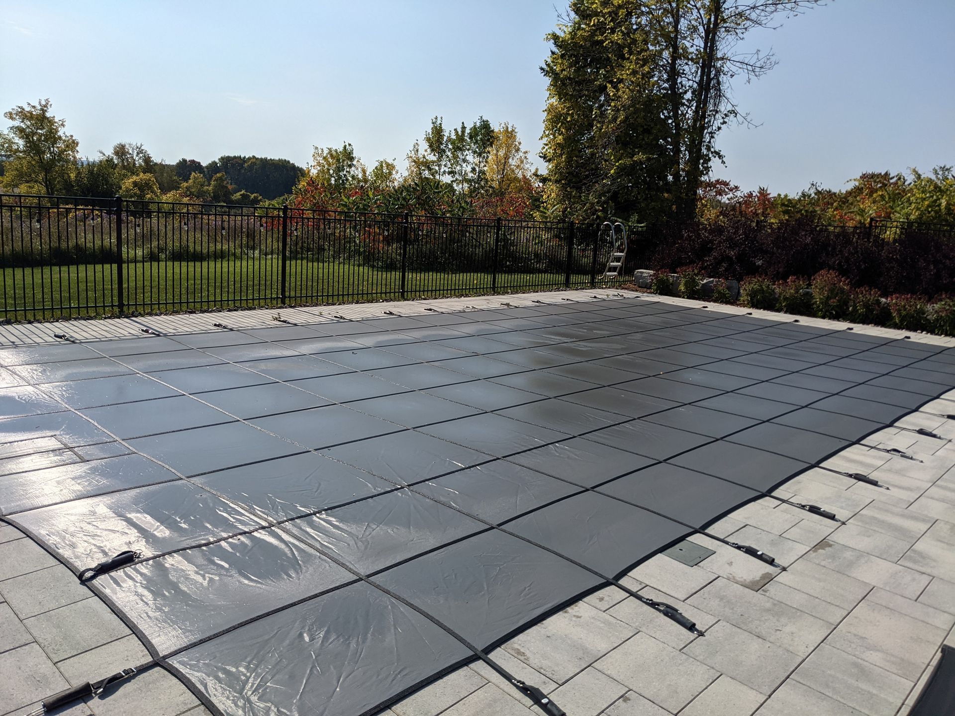 Grey pool cover over a rectangular pool on a patio.