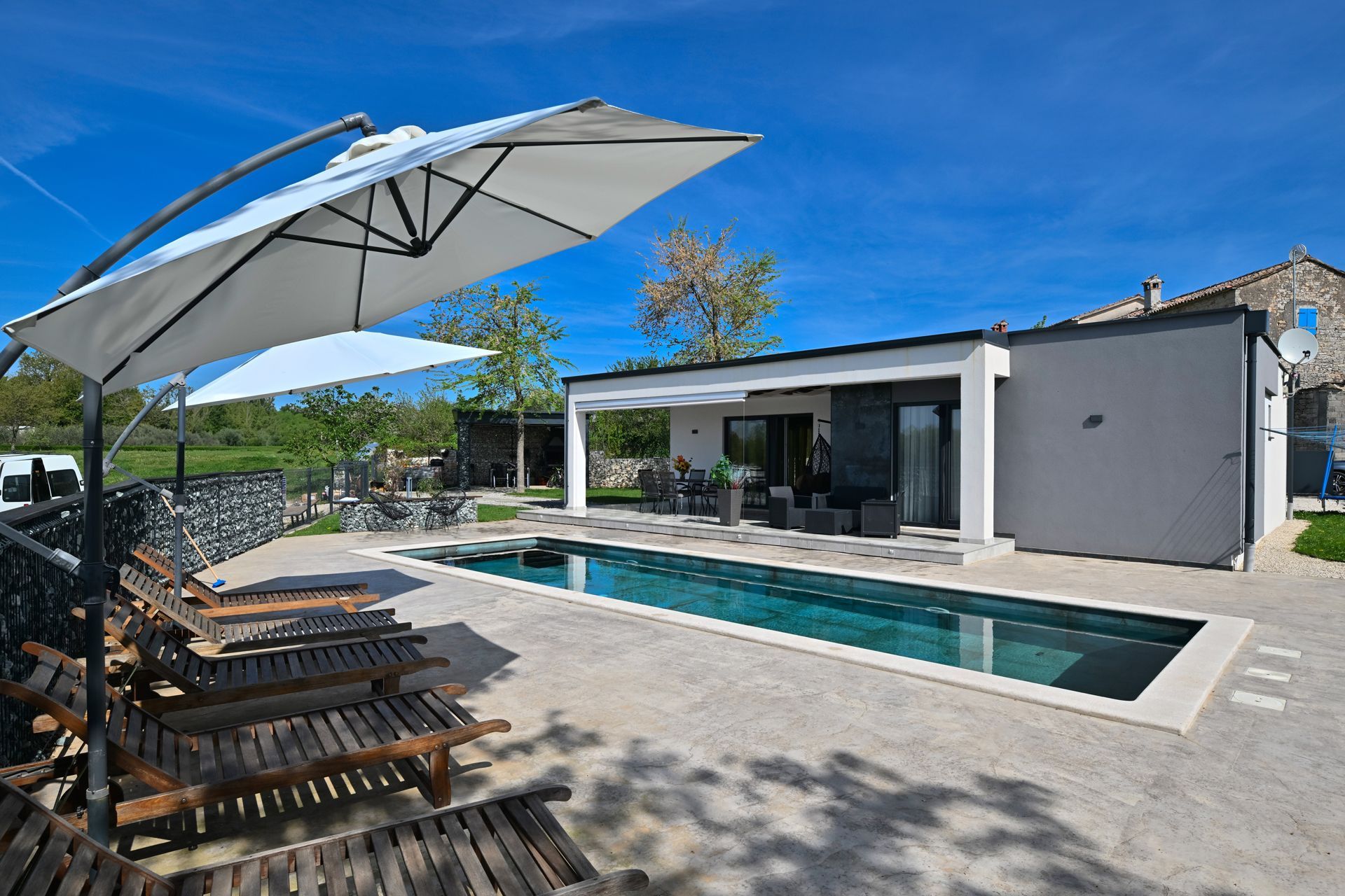 Swimming pool and modern villa with lounge chairs, umbrella, and a blue sky.
