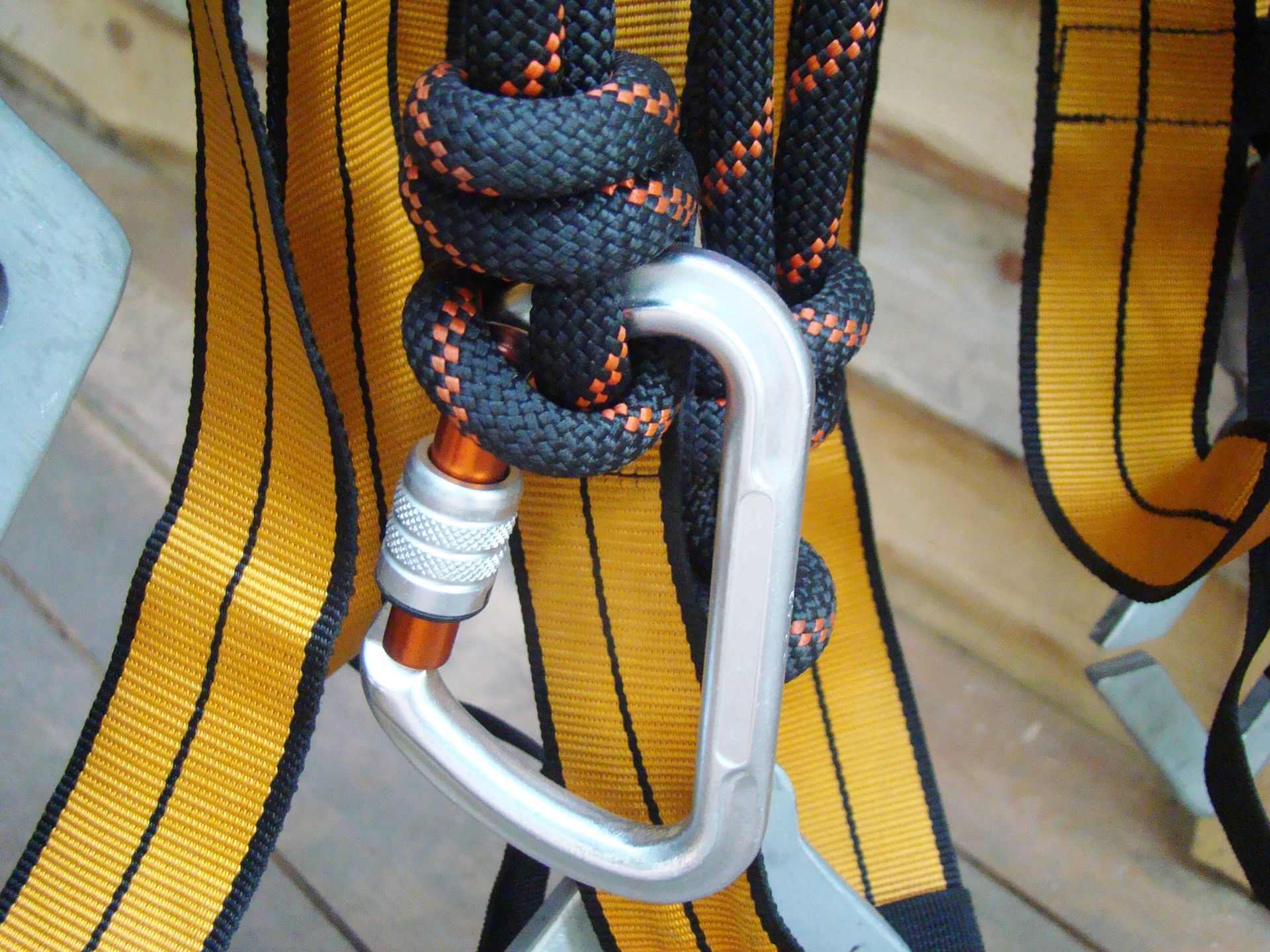 Arnés de escalada con cuerda negra y naranja asegurado con un mosquetón plateado.