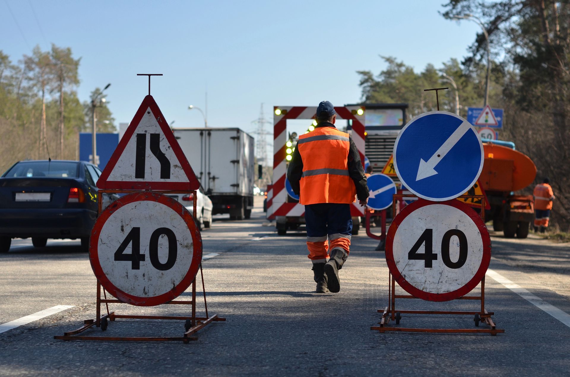 Obras en la carretera: Un trabajador con chaleco naranja se encuentra en una autopista con tráfico.