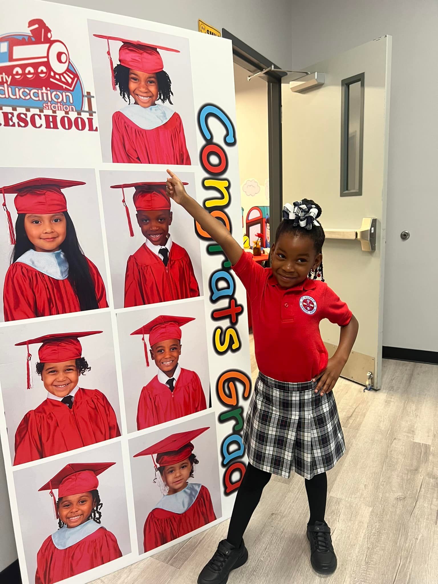 A little girl is standing in front of a graduation poster.