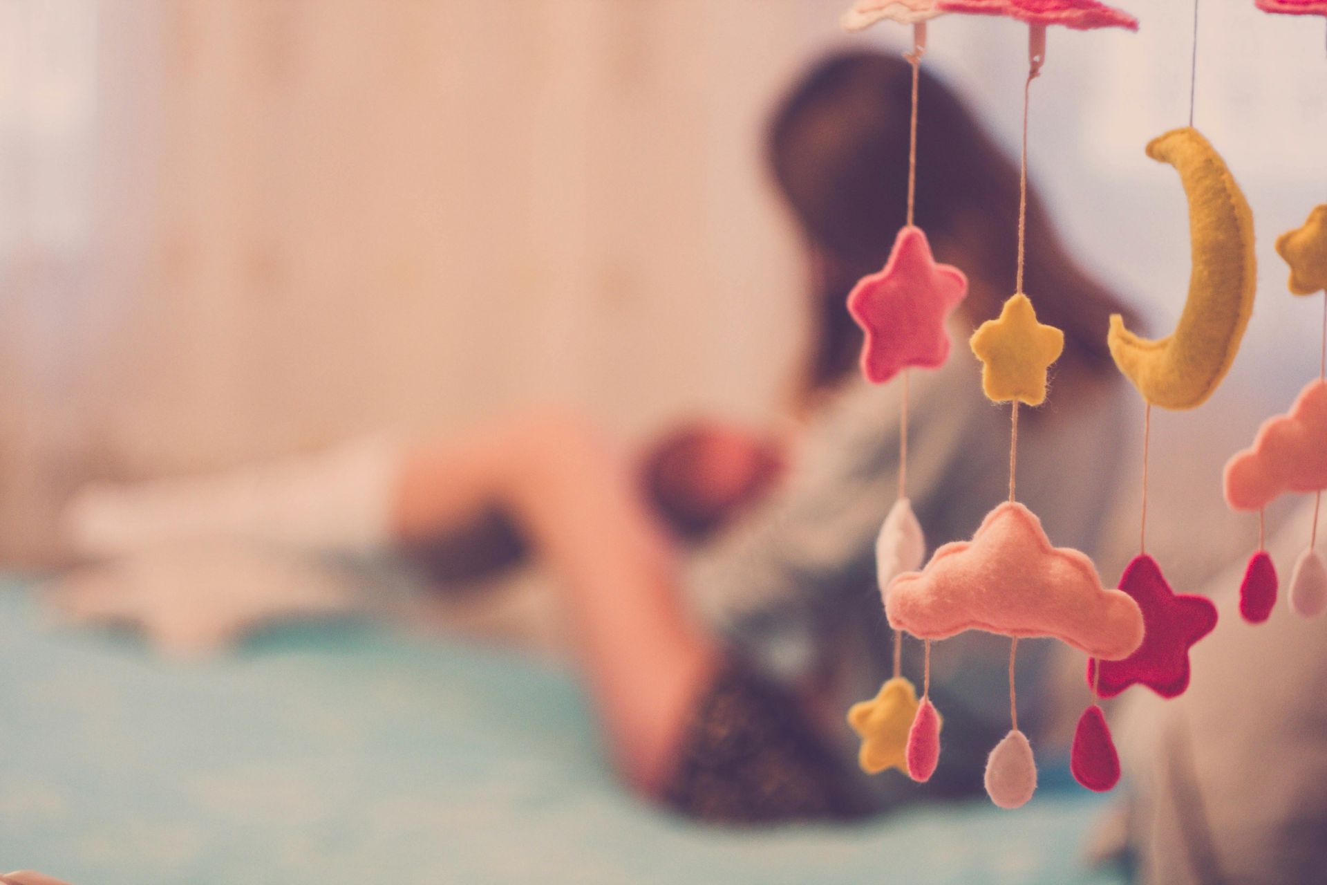 A woman is breastfeeding a baby on a bed with a mobile in the foreground.