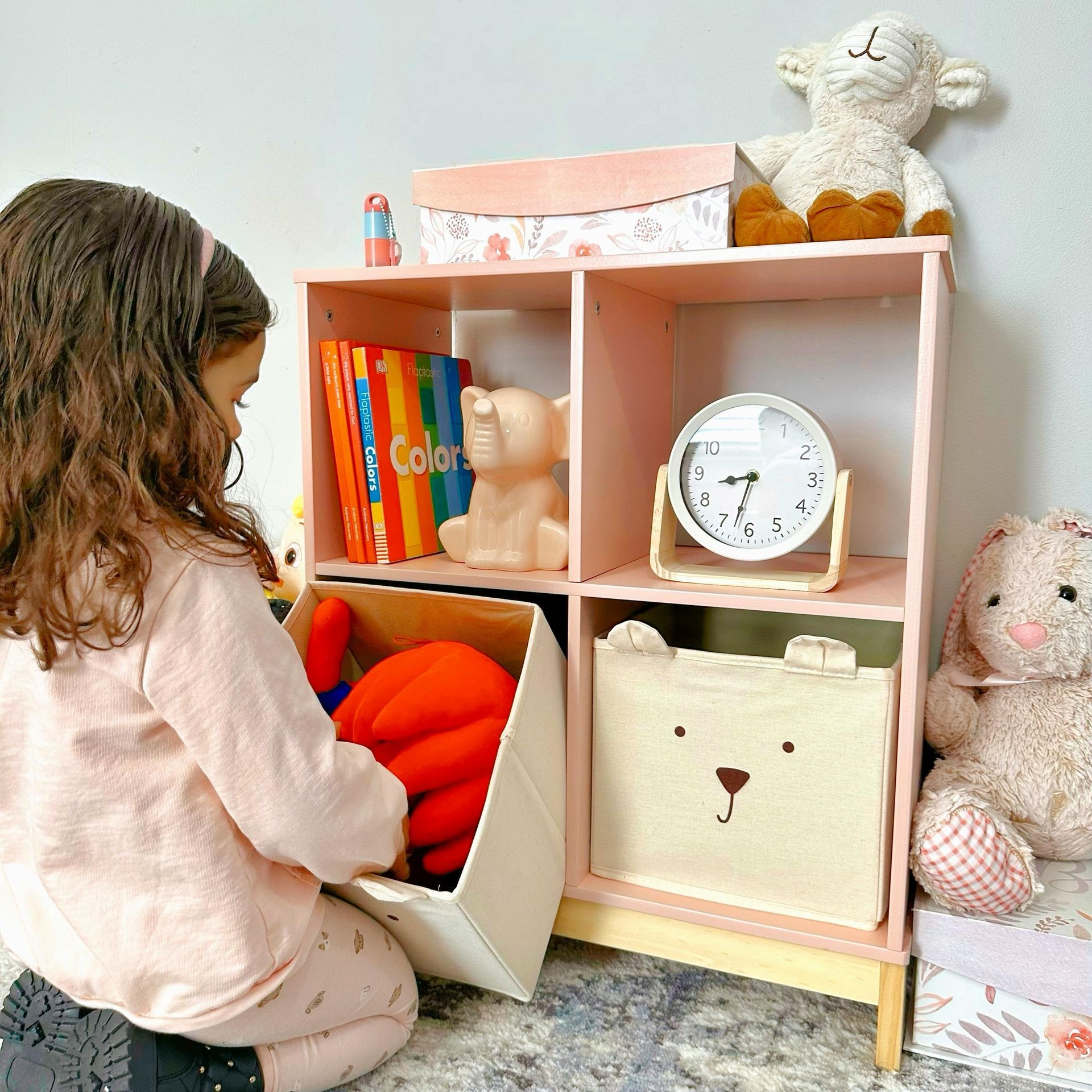 A little girl is kneeling down in front of a bookshelf filled with stuffed animals.