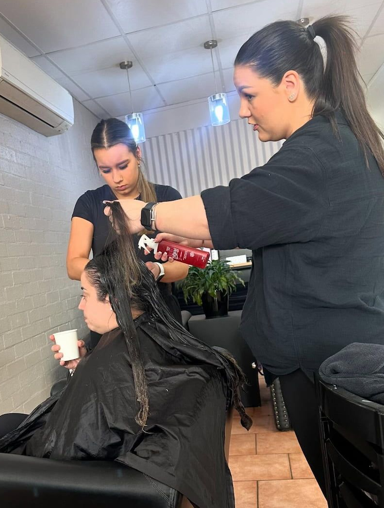 Two Stylists Working Together to Apply Hair Product to a Client Sitting — Devyani Hair & Beauty in Unanderra, NSW