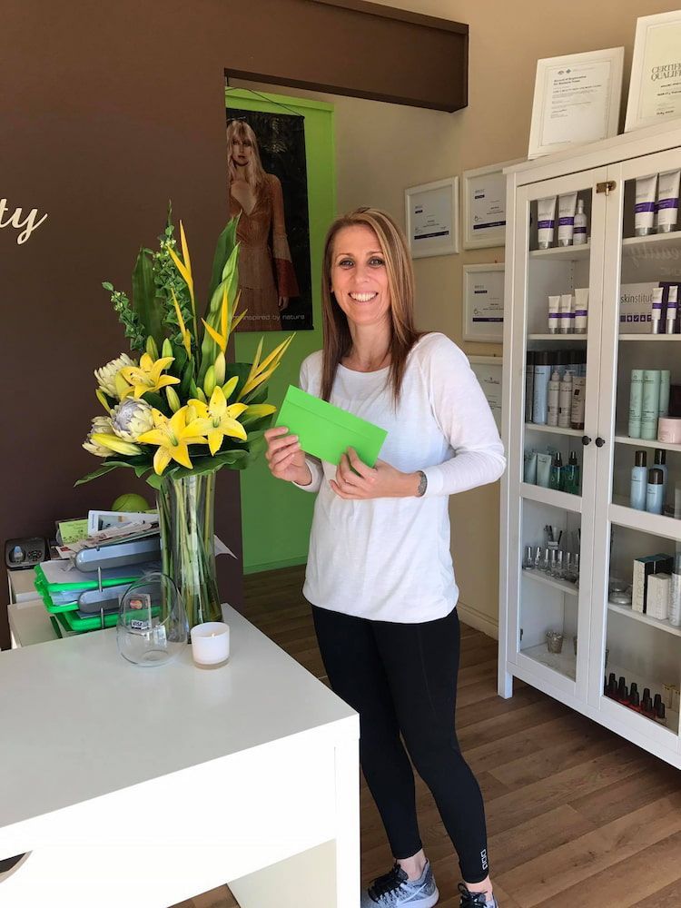 A Smiling Person Stands in a Spa Holding a Green Envelope — Devyani Hair & Beauty in Unanderra, NSW