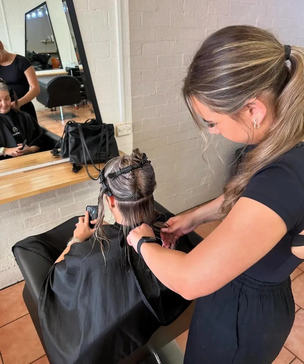 A Stylist in a Black Top Uses Scissors to Trim Hair — Devyani Hair & Beauty in Unanderra, NSW